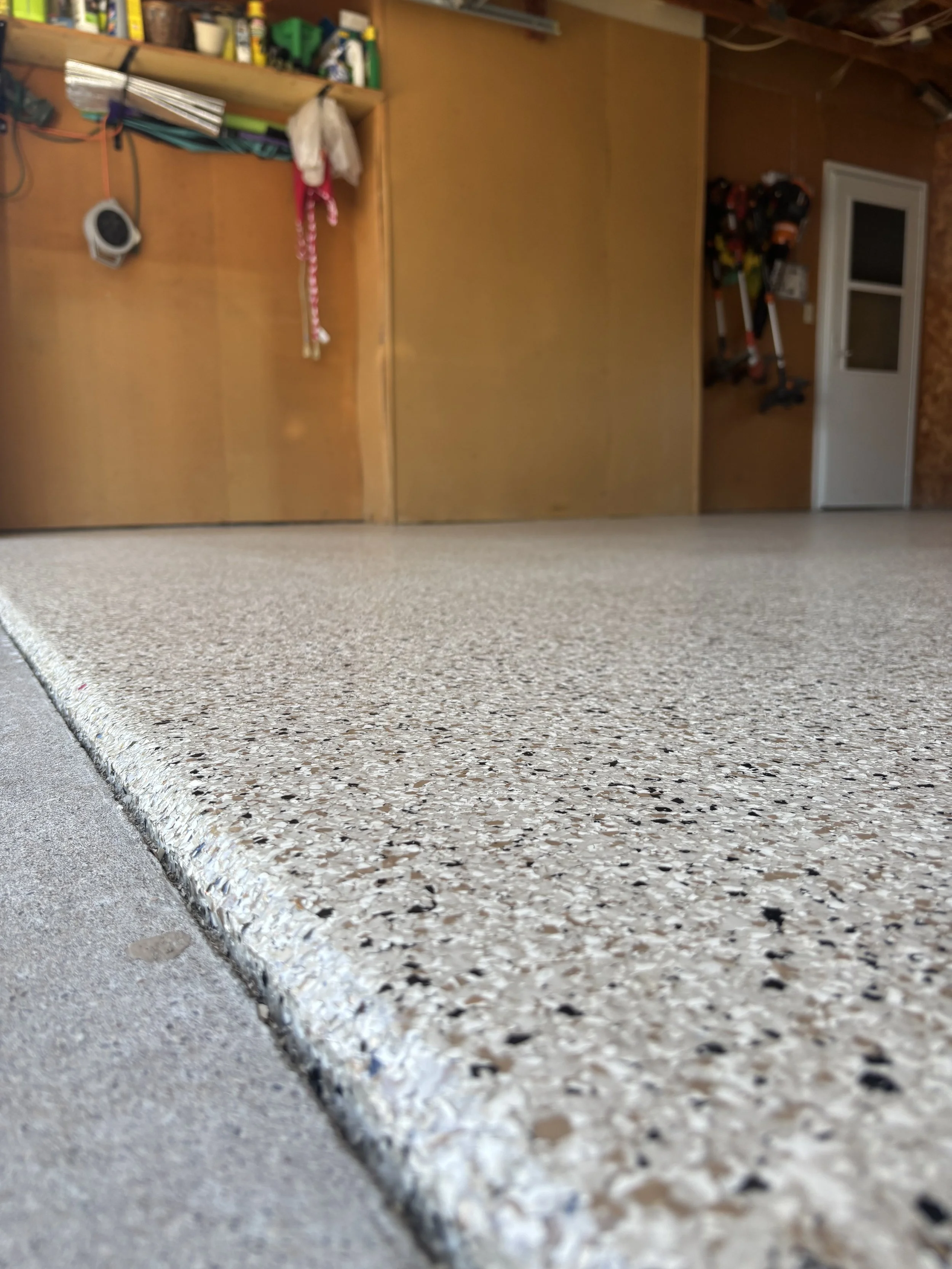 Close-up of a speckled beige and black countertop with a sharp edge, local home workshop with wooden shelves, various tools, and equipment in the background.