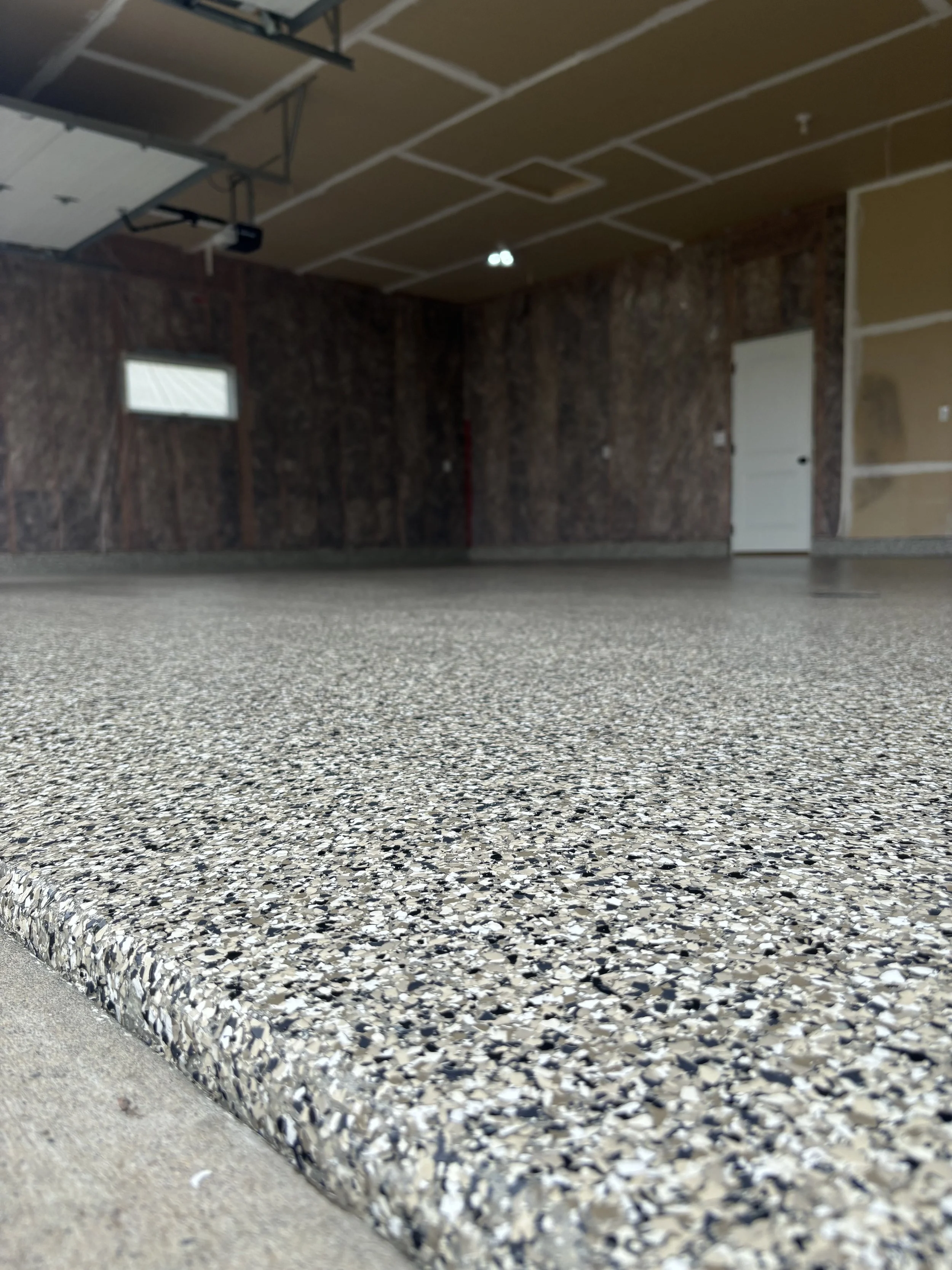Close-up of a granite step with a speckled pattern, leading to an unfinished interior space with a concrete floor, brick wall, and a partially installed ceiling.