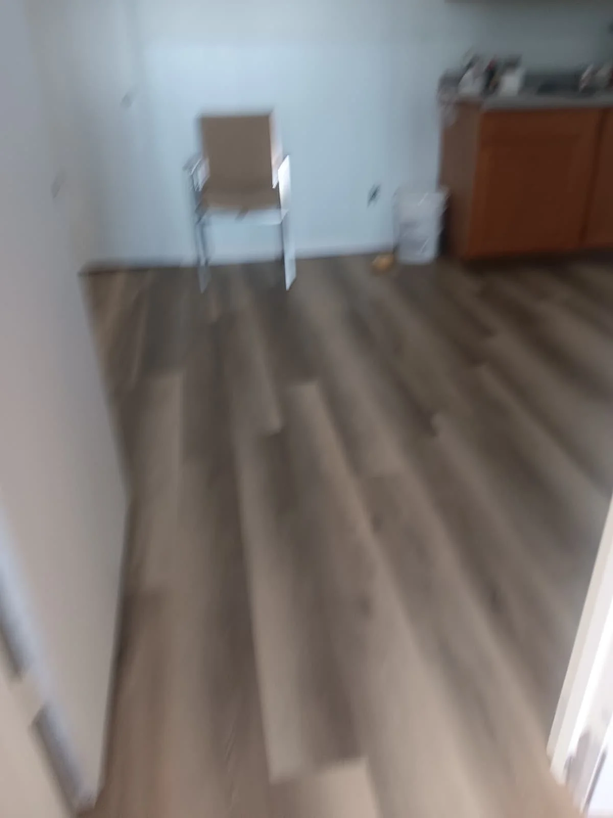 A blurry image of an indoor room with wooden floors, a wall with a chair, some cabinets, and indistinct objects.