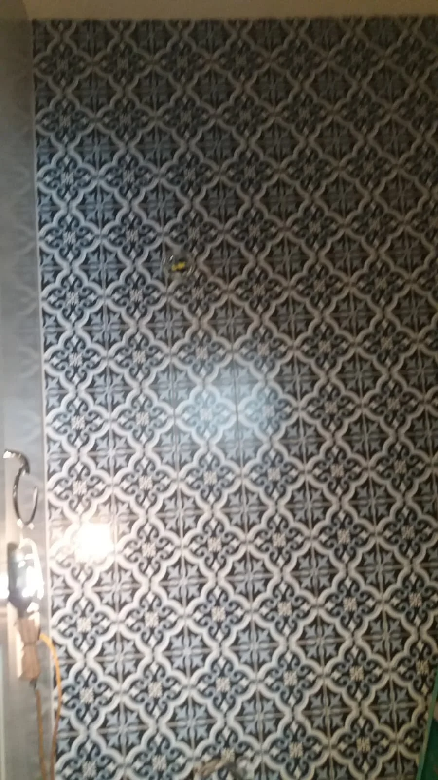 Patterned black and white decorative tiles on a wall, with a light fixture and some electrical cords partially visible on the left side.
