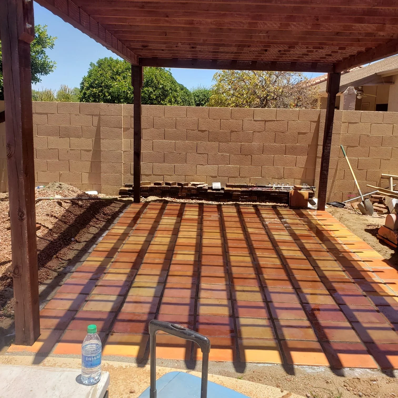 Under construction outdoor patio with a pergola, brick flooring, and a brick wall background. Construction tools and materials are visible.