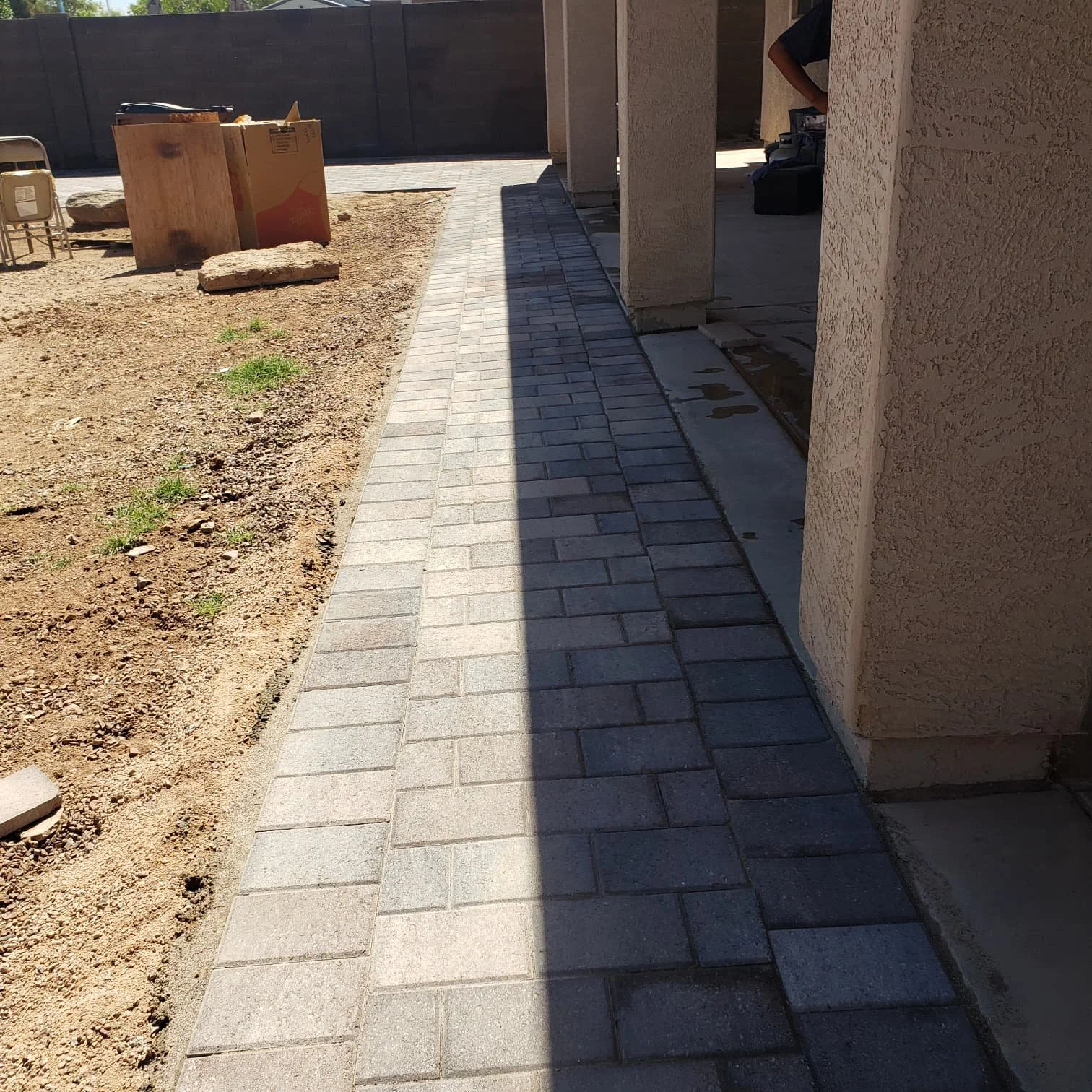 Newly installed brick sidewalk next to a house under construction, with dirt and construction materials nearby.