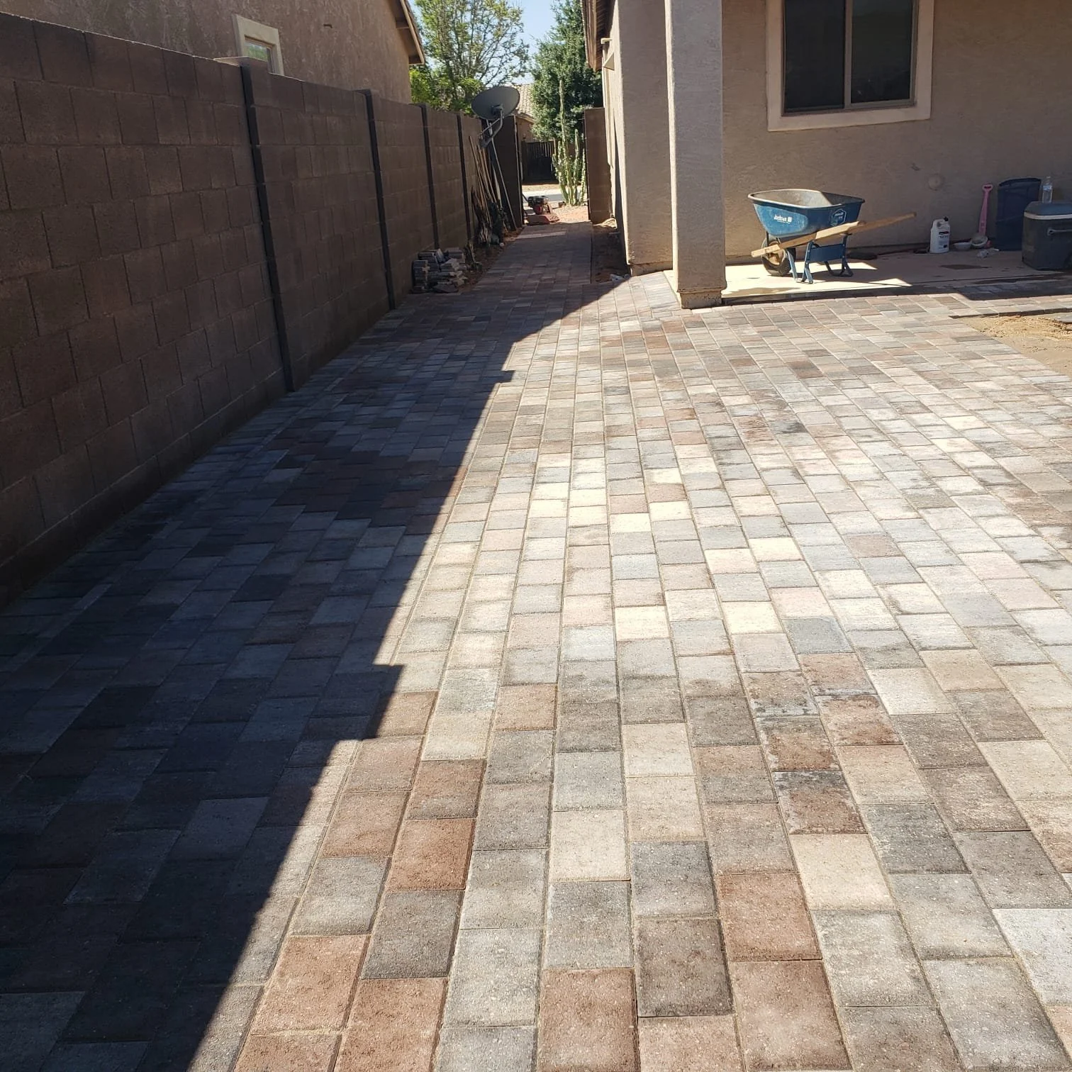 A newly paved brick patio with a stone wall on the left and a house on the right, showing the ongoing construction of a backyard.