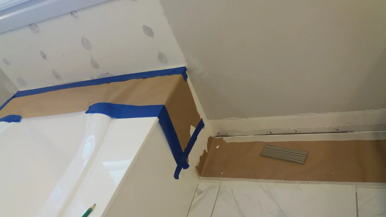 Part of a room under renovation with masking tape and protective paper on the floor and walls, near a vent on the baseboard.