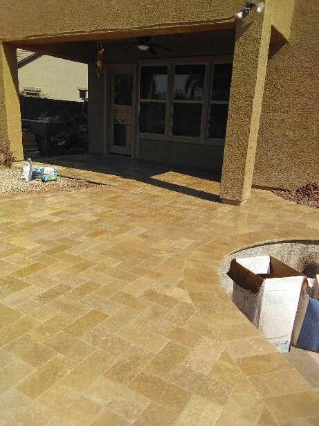 Patio area with tile flooring, a house entrance with a porch, and a partially visible tree planting area with a circular border.