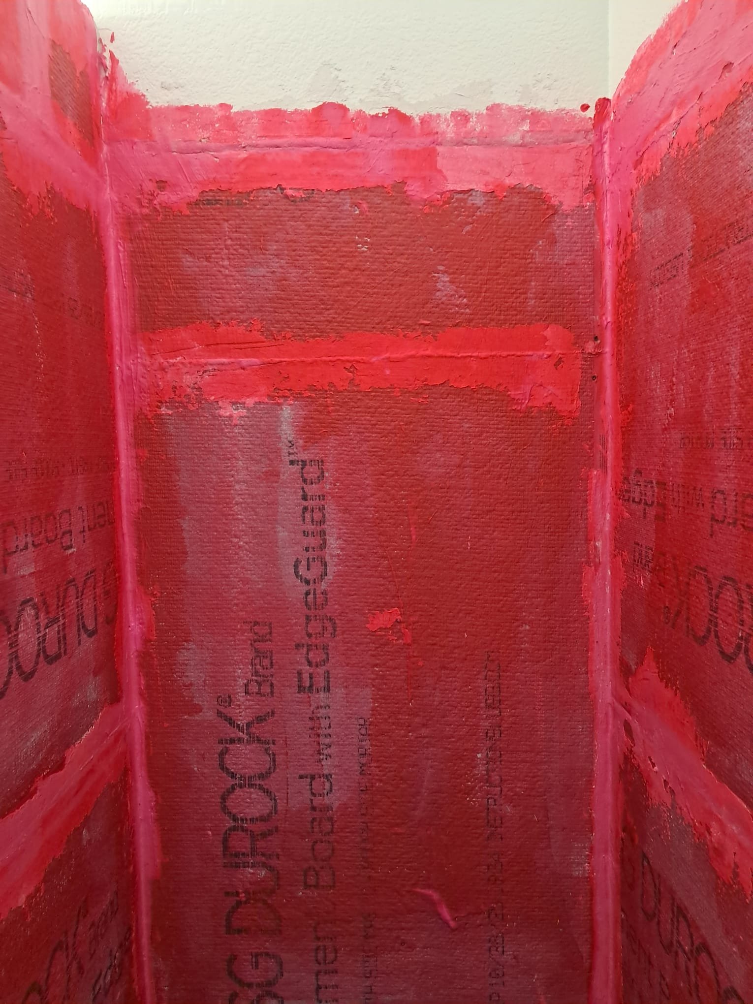 Interior of a wall with red insulation and drywall. The insulation is red and the drywall is partially installed with some exposed areas.