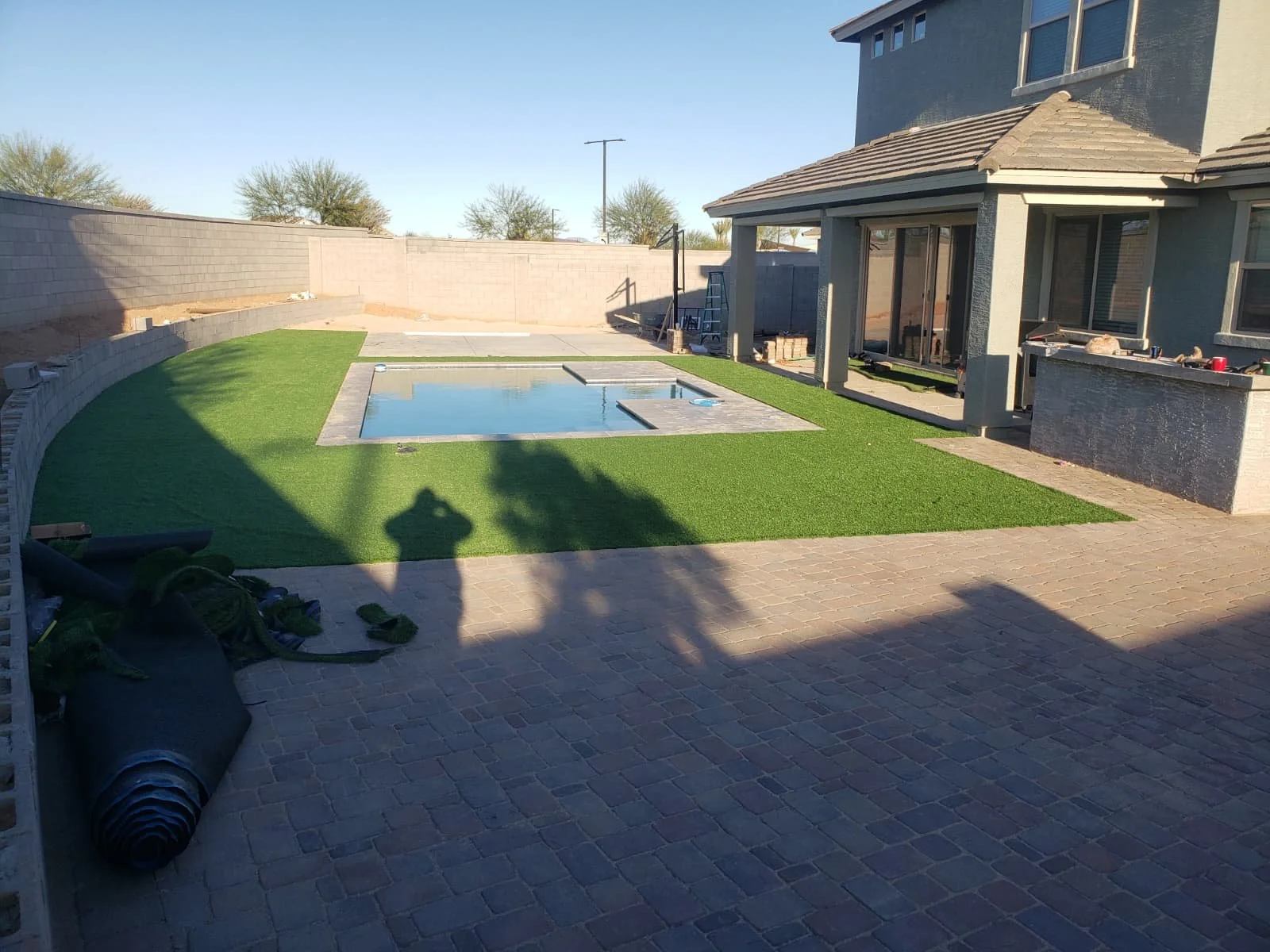 Backyard patio with a partially completed swimming pool, artificial grass, and a house with large sliding glass doors.