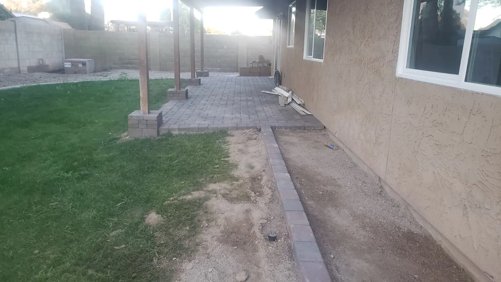 Backyard patio in progress with installed pavers, new brick wall section, and construction materials on the ground.