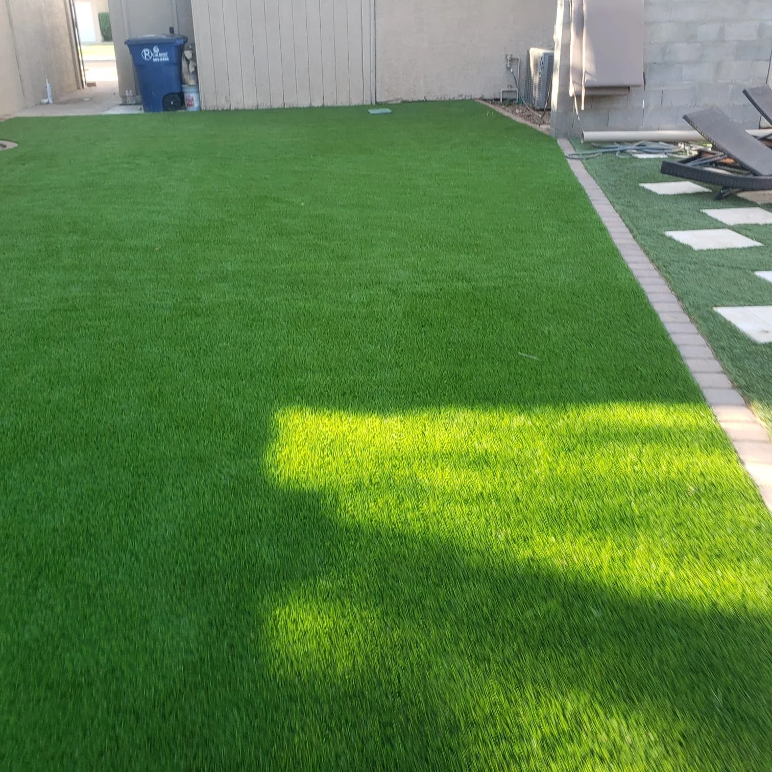 Artificial grass lawn with a shadowed area and a small section of stone pathway on the right side.