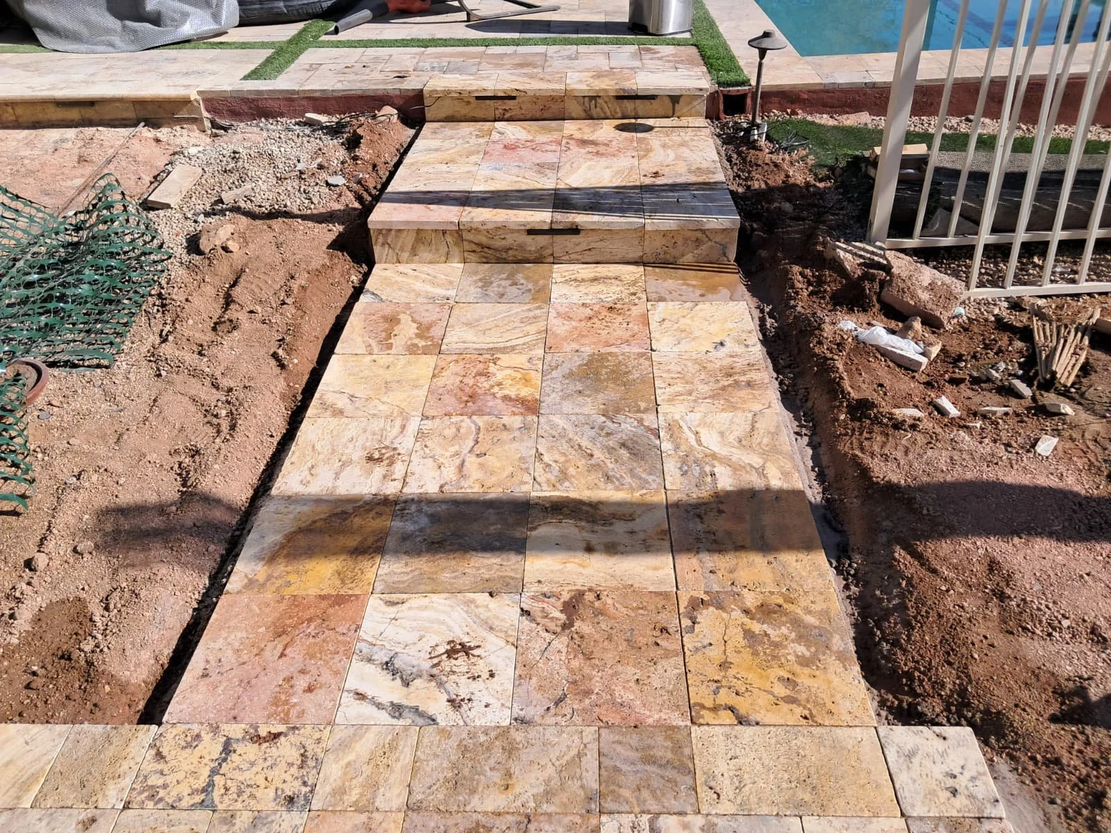 A newly constructed tiled pathway with small steps, surrounded by construction dirt and unfinished landscaping.