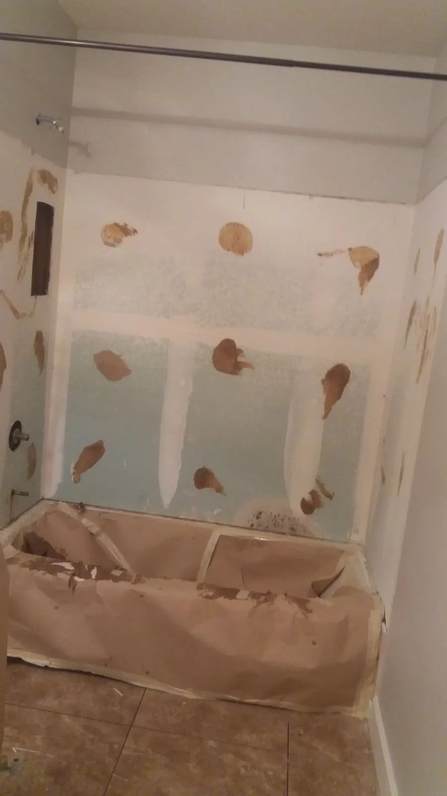 Bathroom with drywall patches and missing tiles on the bathtub surround, taped off for renovation or repair.