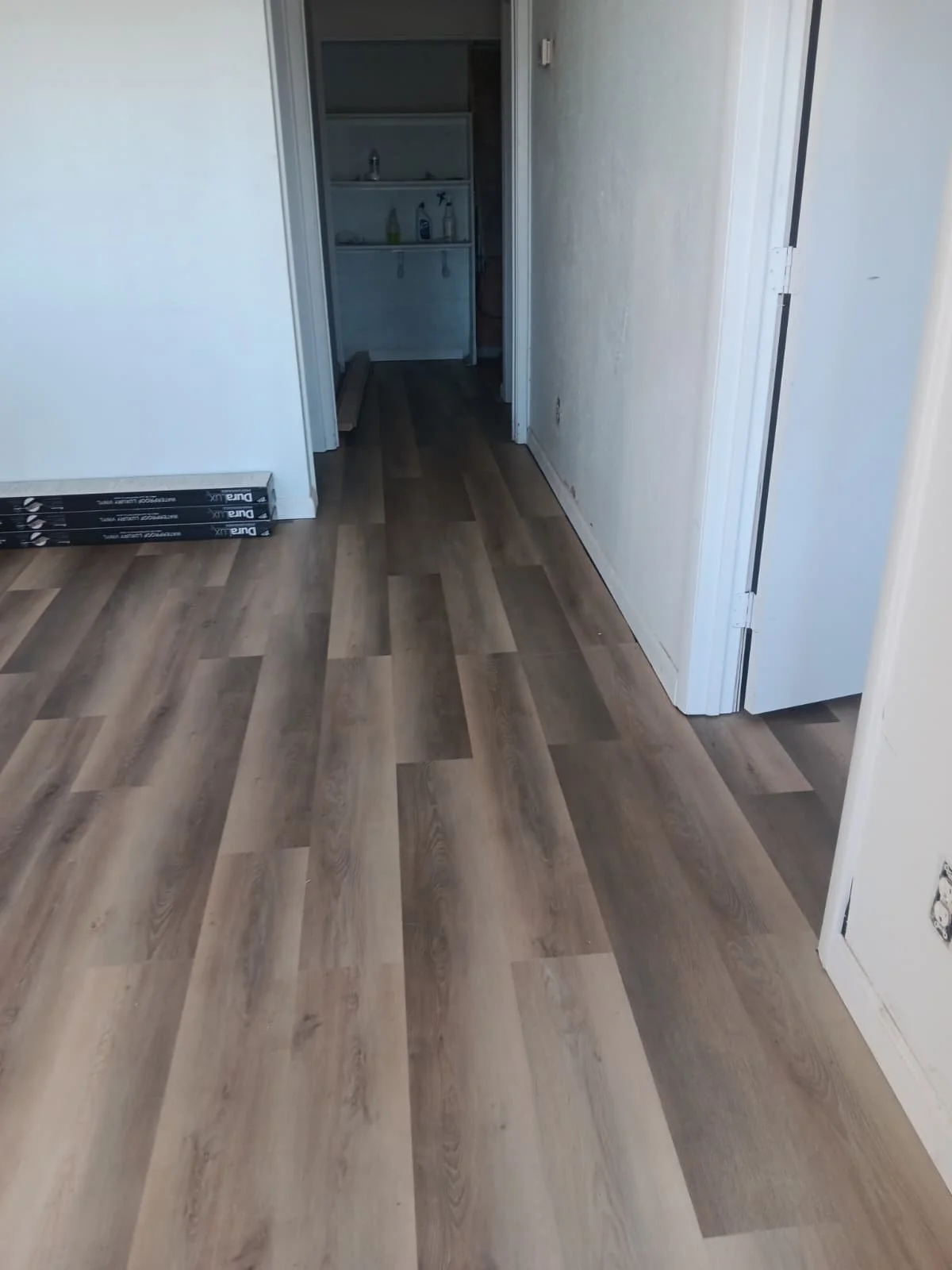 Newly installed wood-look vinyl flooring in a hallway leading to a small laundry area with a sink and cleaning supplies.