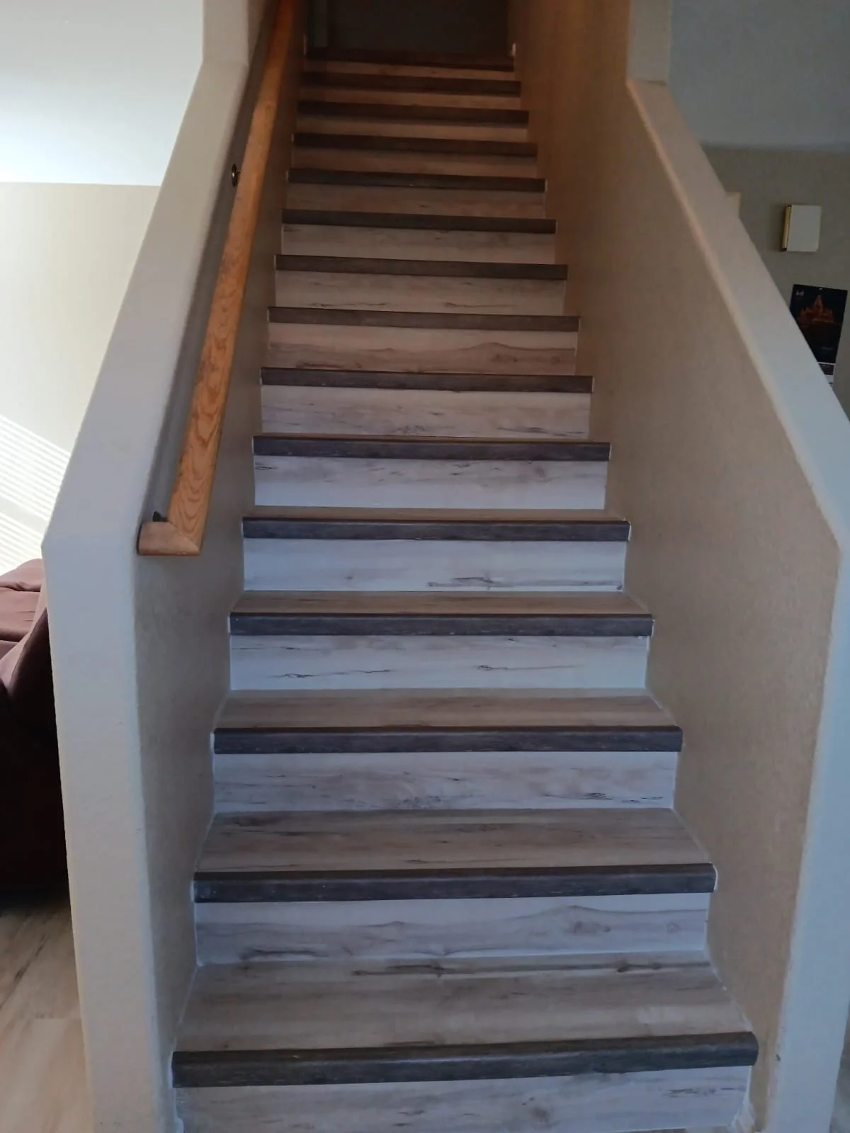 Wooden stairs with a wooden handrail on the left side, ascending to an upper floor inside a house.