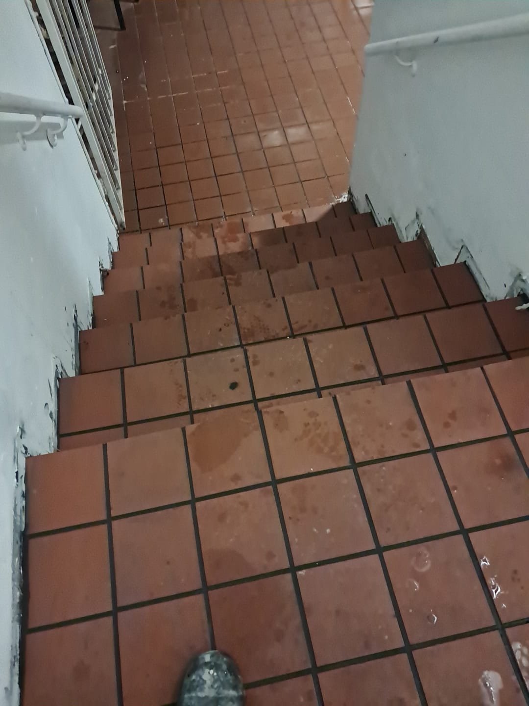 Wet brown tile staircase with water puddles and a person’s muddy shoe visible at the bottom.