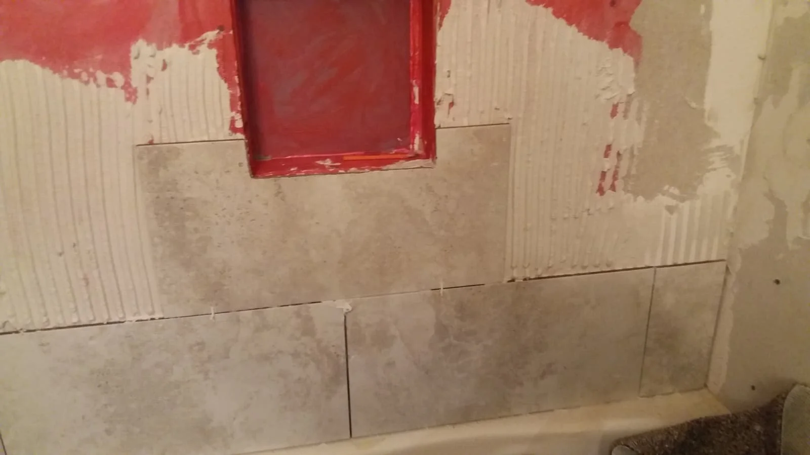 Bathroom wall with tiles and red-painted plumbing access panel.