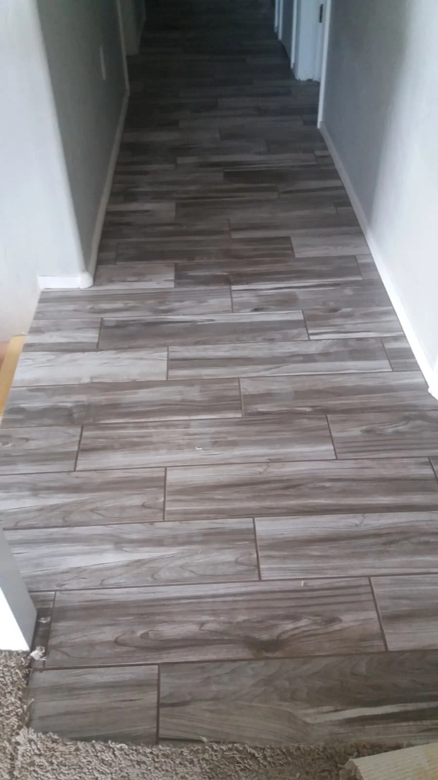 A hallway with wood-look tile flooring that is gray and brown, leading into a darker area.