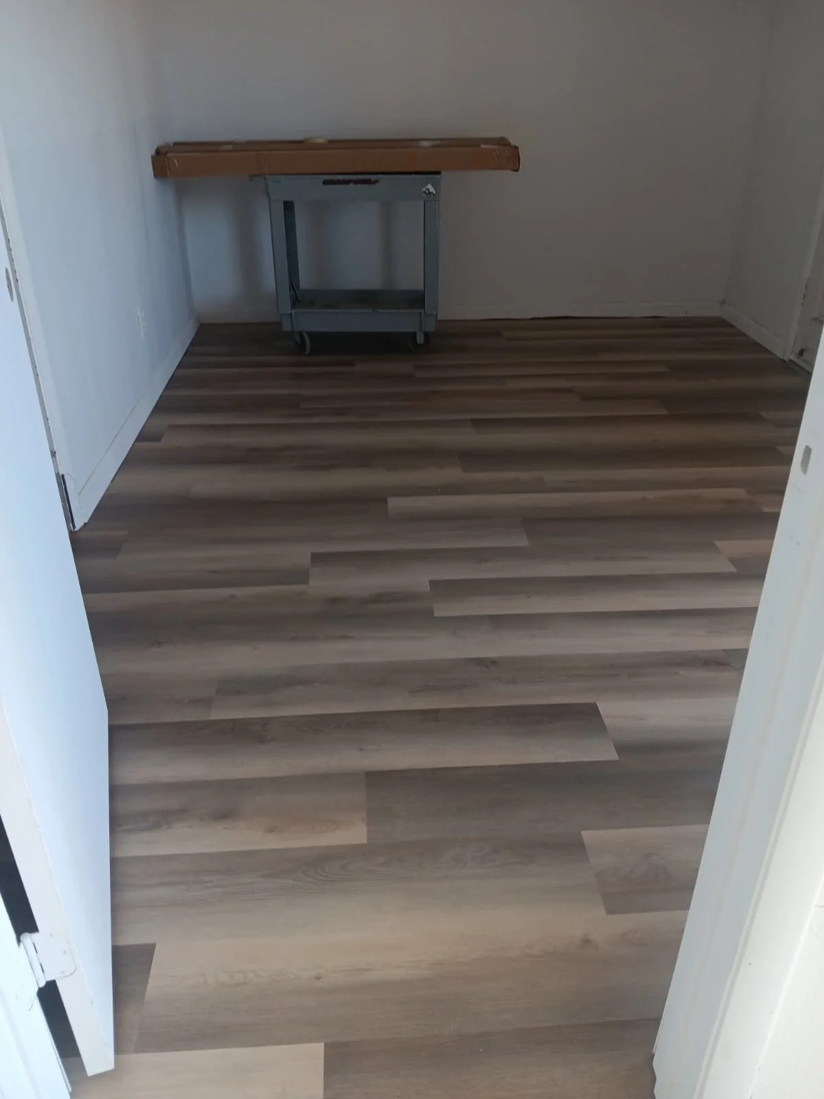Empty room with wood laminate flooring, white walls, and a small table at the far end.