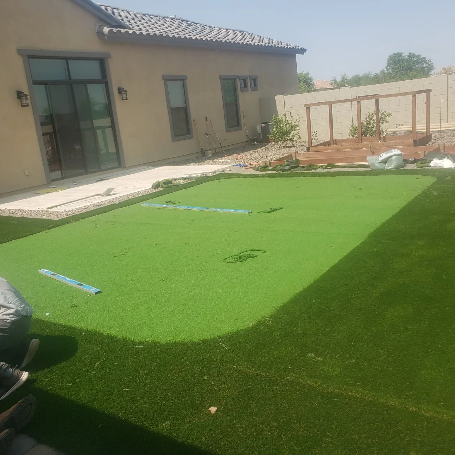 Backyard with a patch of artificial grass, construction tools, and a partially built wooden deck in the background.