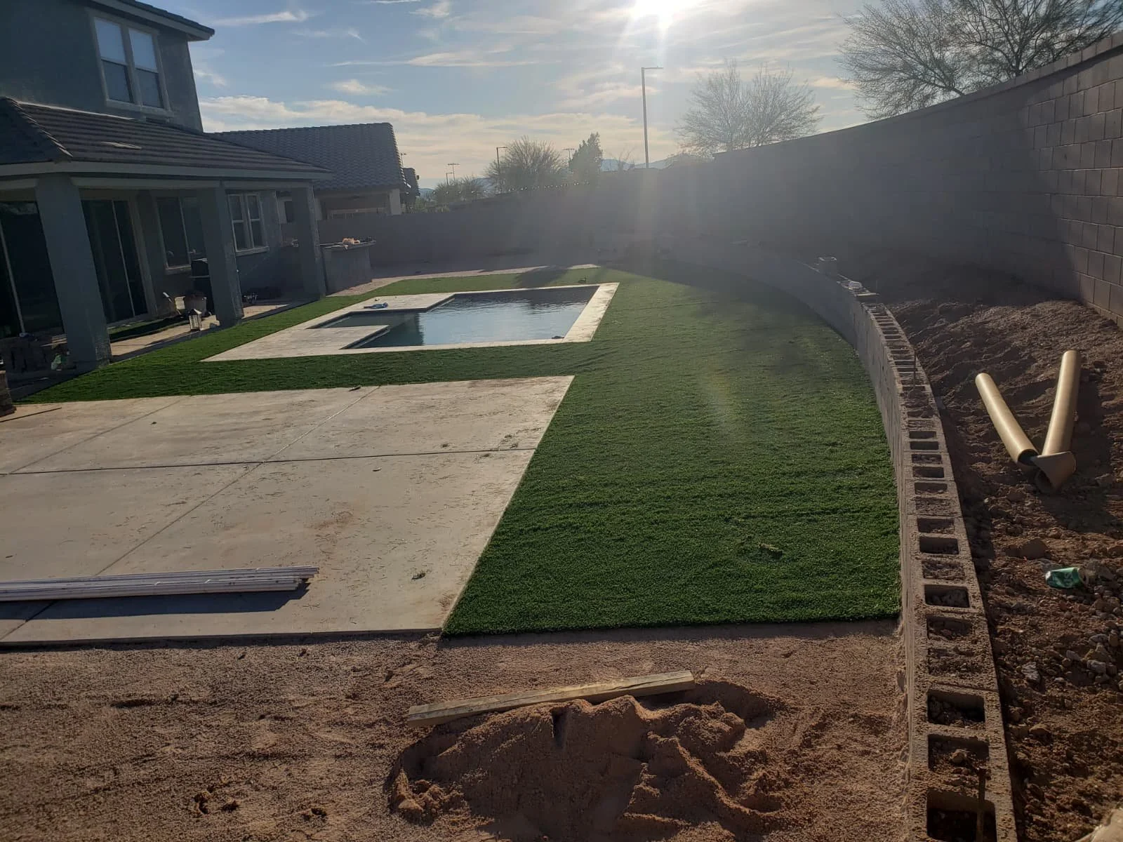 Backyard with a swimming pool, artificial turf, and a partially built brick fence in progress.