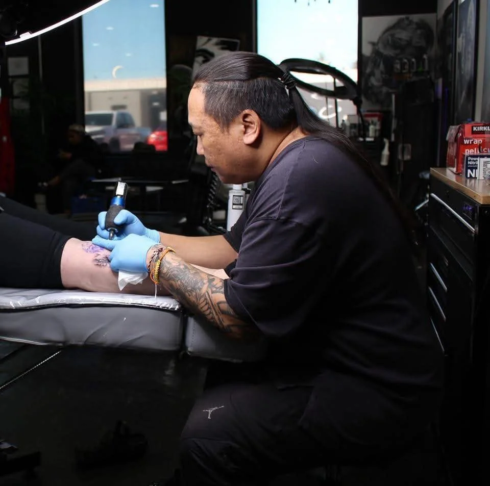 Tattoo artist drawing on a person's ankle in a tattoo studio.
