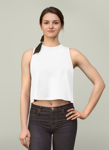Young woman with long brown hair tied in a braid, wearing a white sleeveless crop top and dark jeans, standing with one hand on her hip against a light gray background.