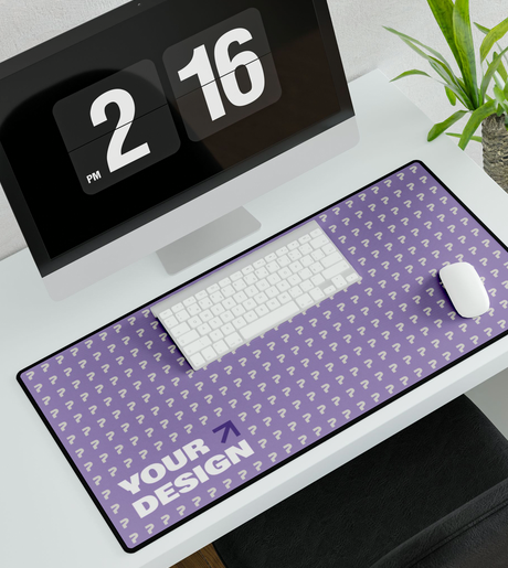 Computer desk setup with a flip clock displaying 2:15 PM, a white keyboard, a white mouse on a purple desk mat with a pattern of white question marks, and a green plant in a pot.
