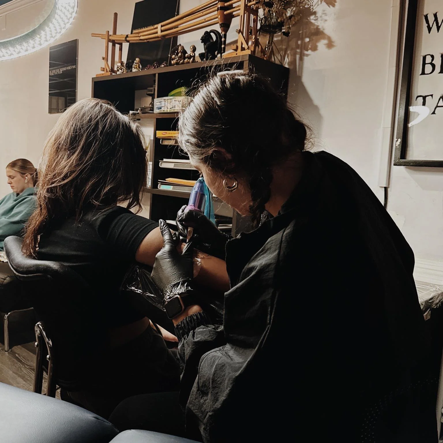 A woman getting a tattoo on her upper arm from a tattoo artist in a tattoo parlor.