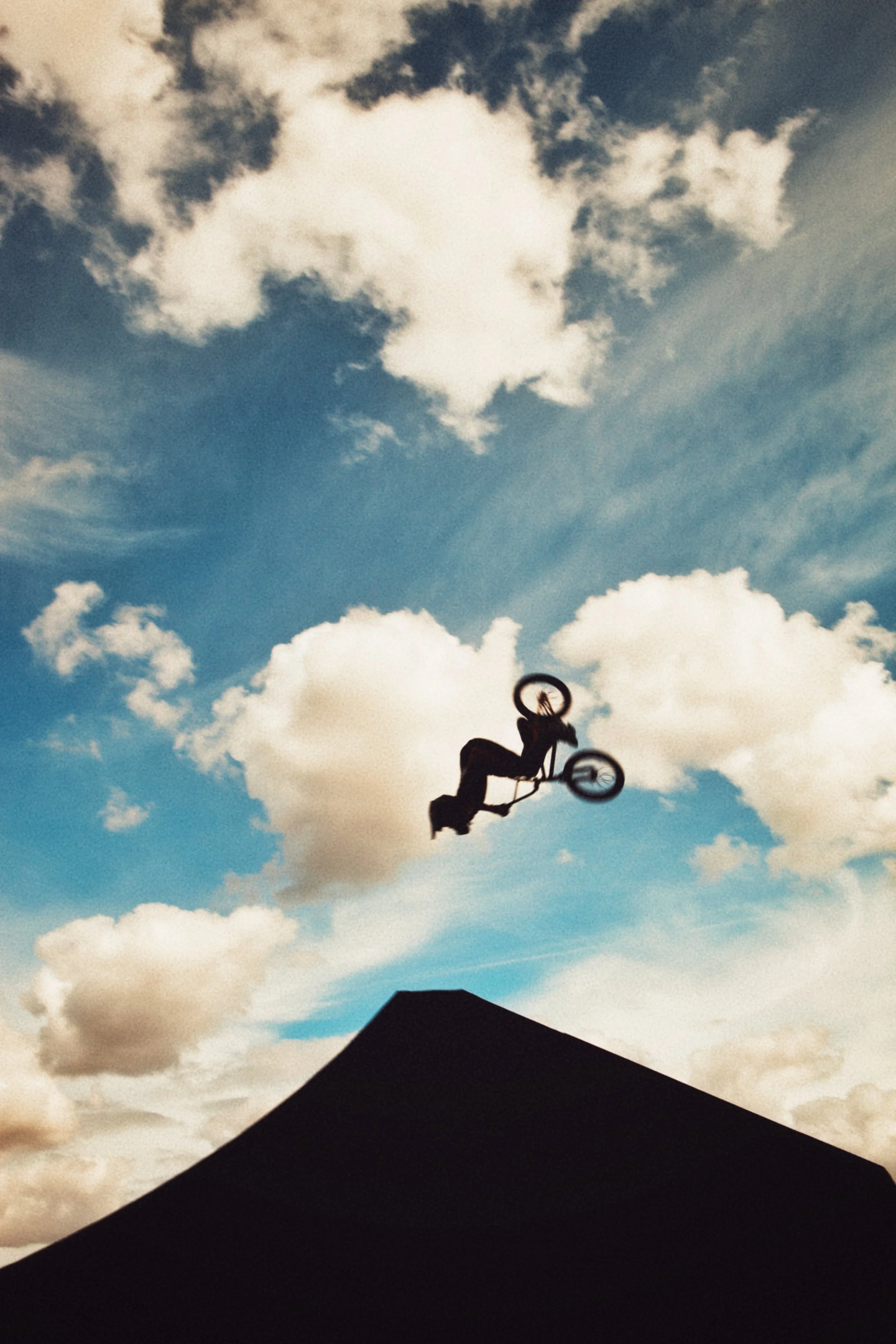 Un jeune homme faisant du vélo dans un saut acrobatique avec un ciel bleu et des nuages en arrière-plan, vue silhouette contre le ciel.