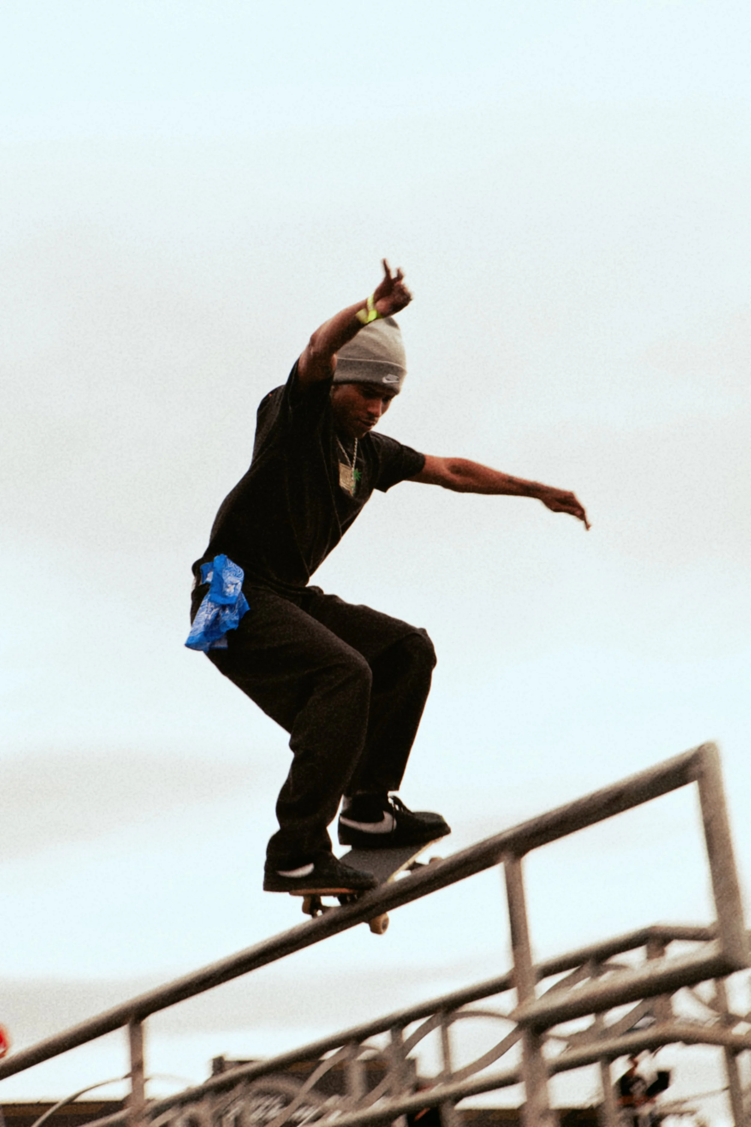 Un jeune homme en roller effectuant une figure sur une rampe de skate, portant un bonnet gris, une chaîne et un t-shirt noir, avec un ciel clair en arrière-plan.