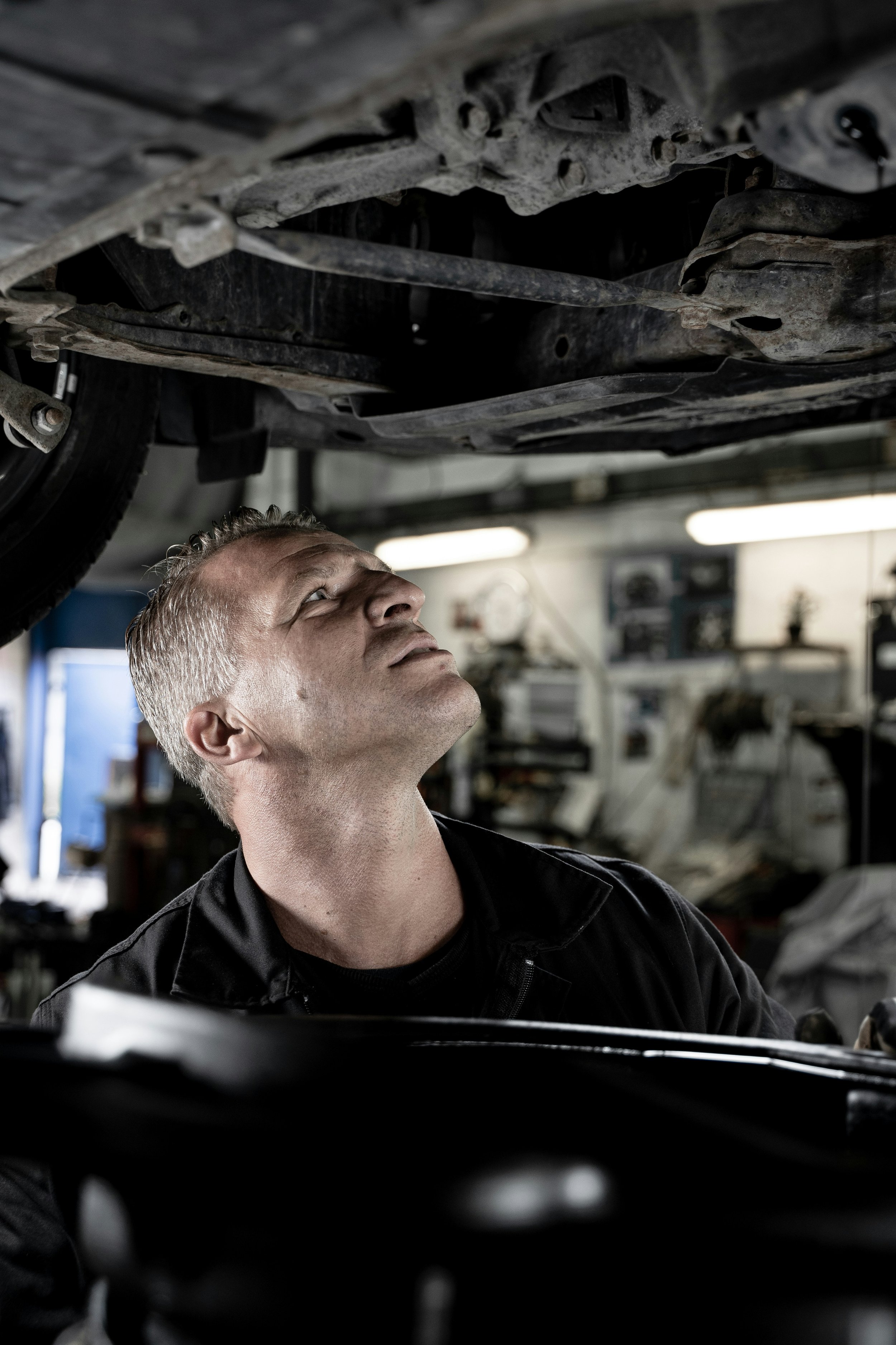 An auto mechanic inspecting the underside of a vehicle in a garage.
