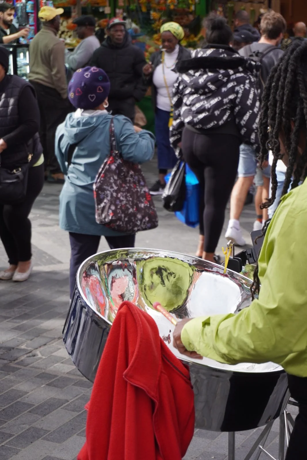 A street musician playing a steel pan at a busy community market, bringing music and cultural energy to shoppers and passers-by.