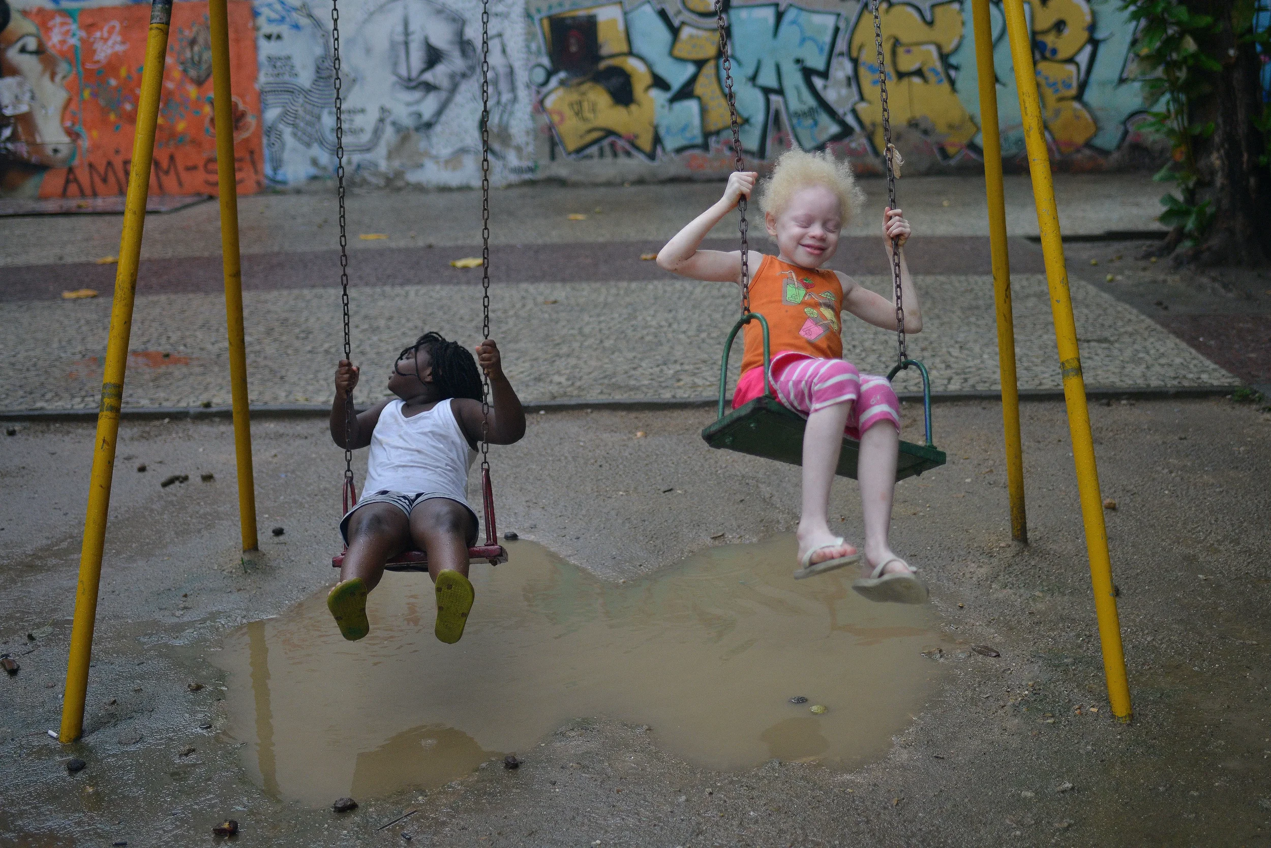 Two young children playing on swings in a public playground, highlighting childhood joy, inclusive play and the importance of equal opportunities for every child.