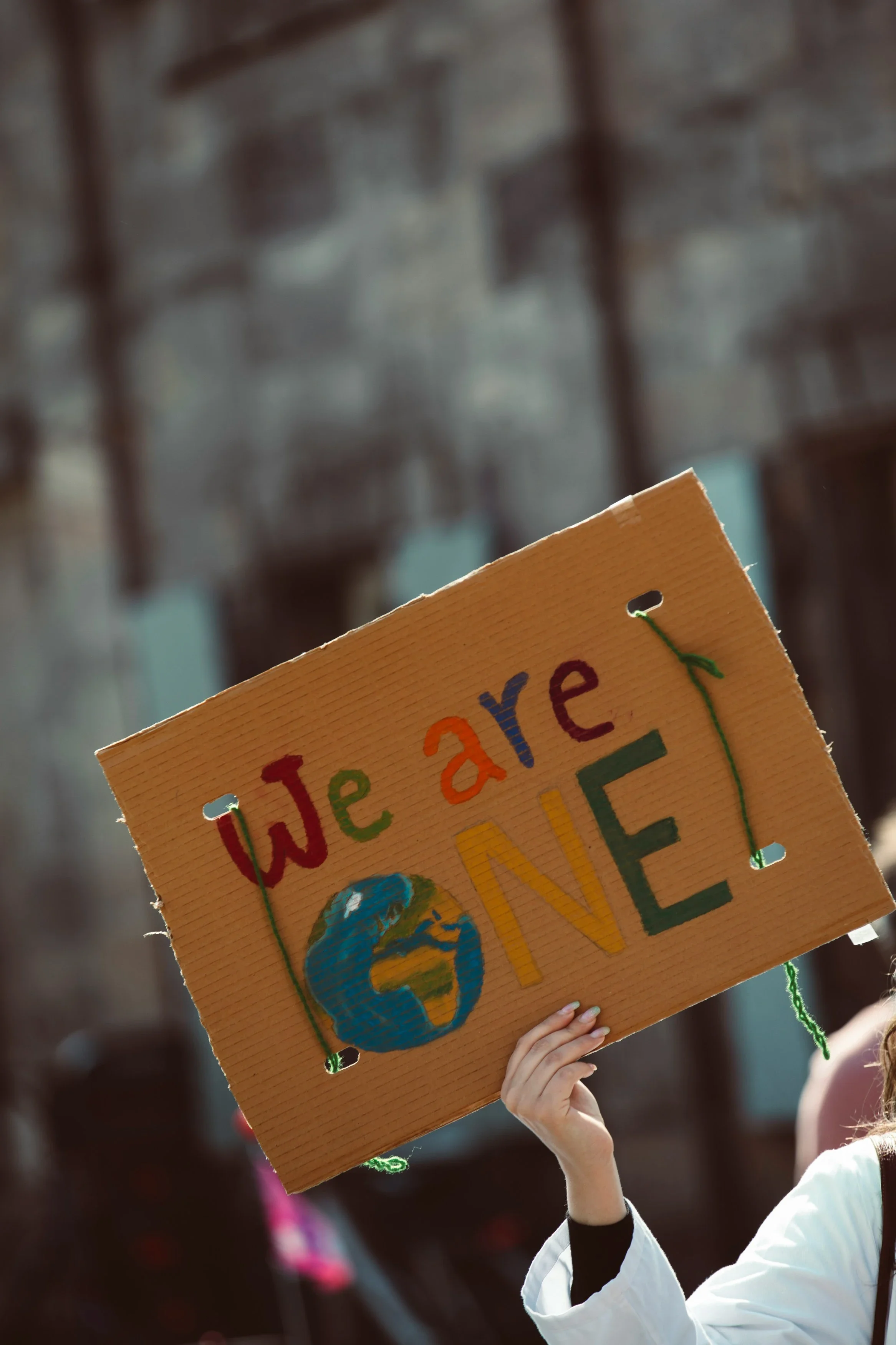 A person holds a handmade cardboard sign reading “We are one,” featuring a painted Earth, symbolising global unity, environmental awareness and collective action.