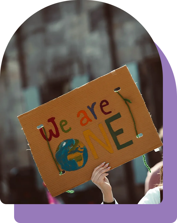 Person holding a cardboard sign that says 'We Are One' with a drawing of the Earth underneath, during a protest or rally.