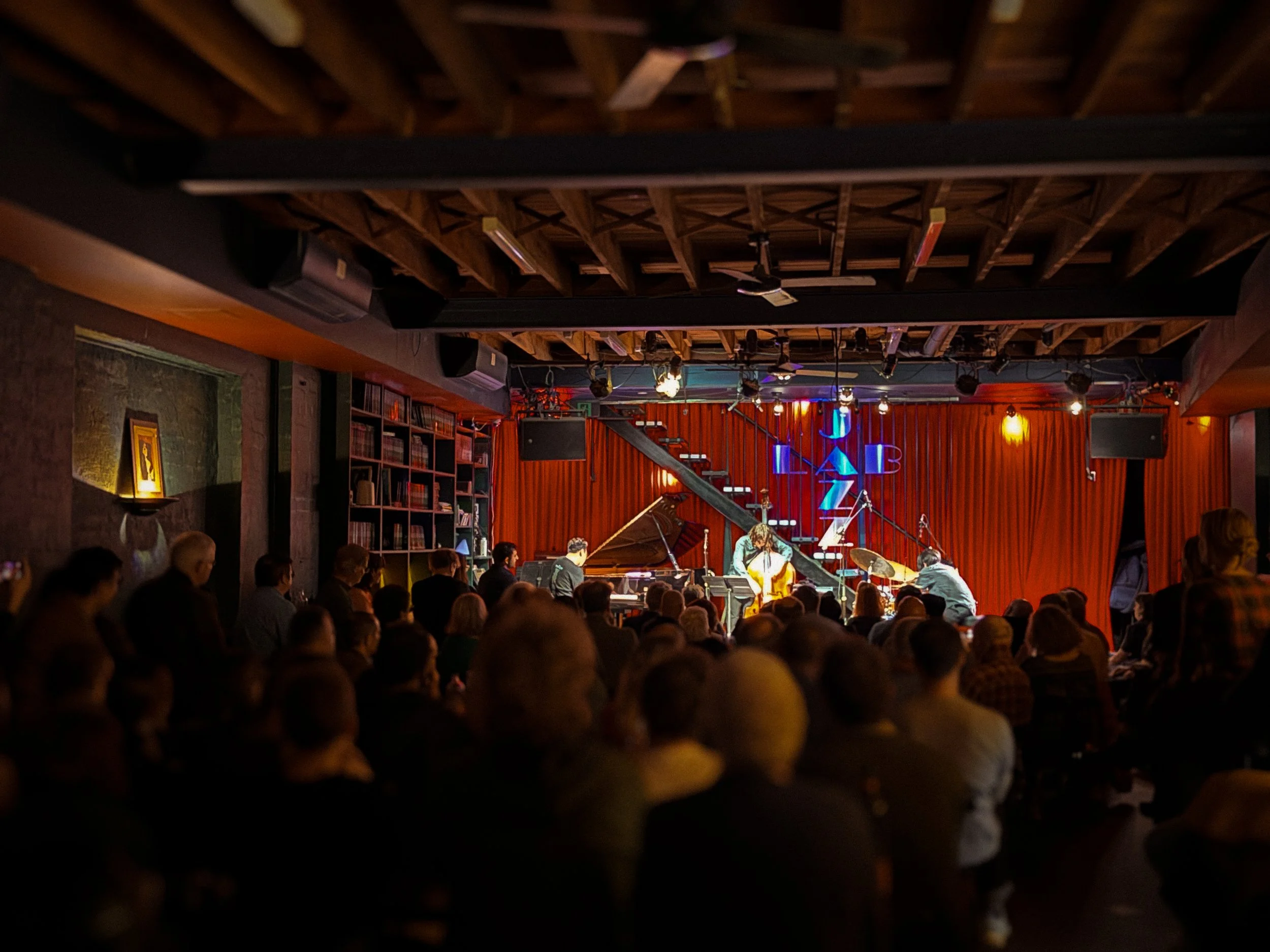 Banksia Trio performing on stage at a club with audience watching.