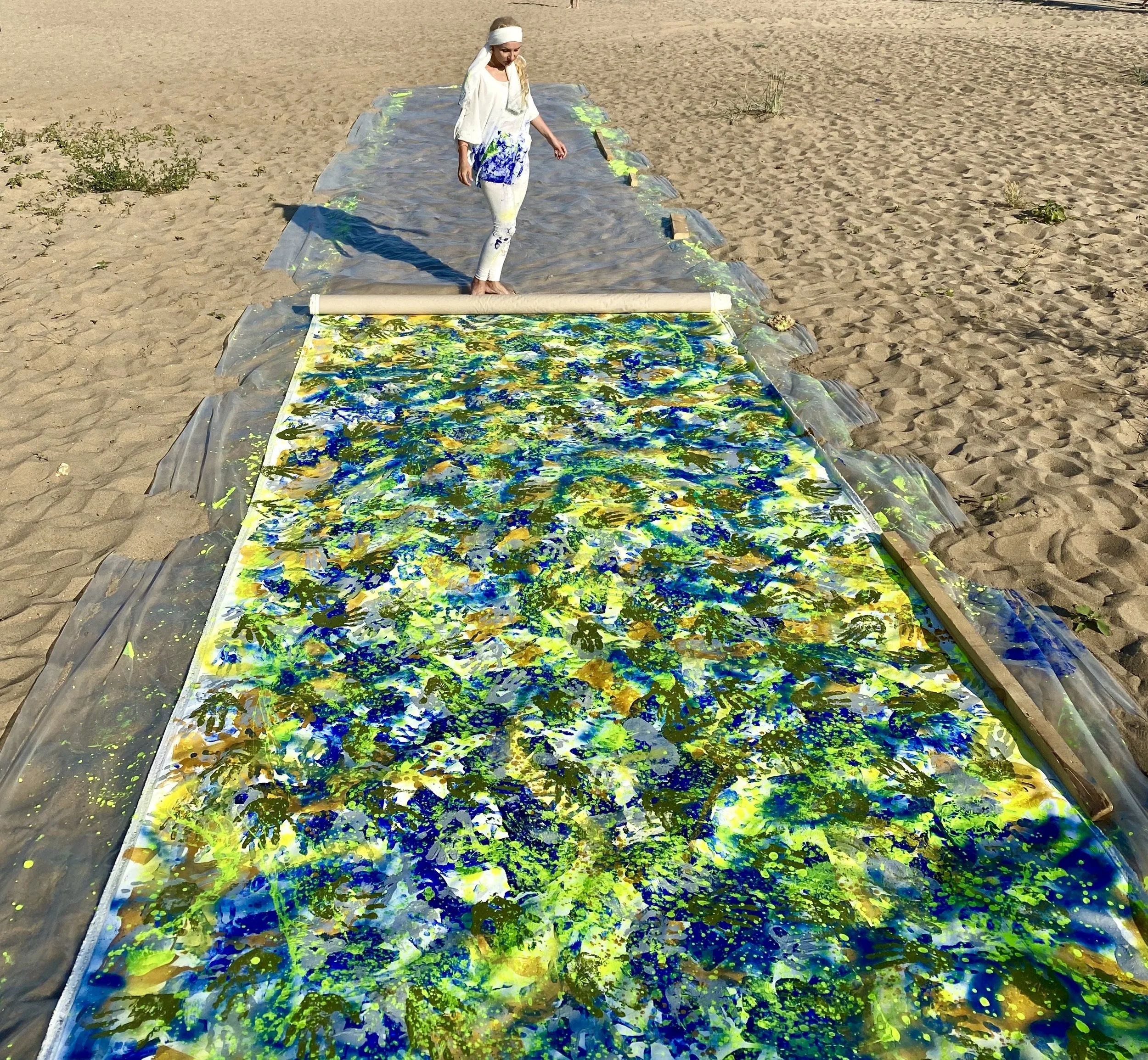 The continuous canvas of Nine extending across the sand, covered with blue, yellow and green paint, with Iryna Sushelnytska