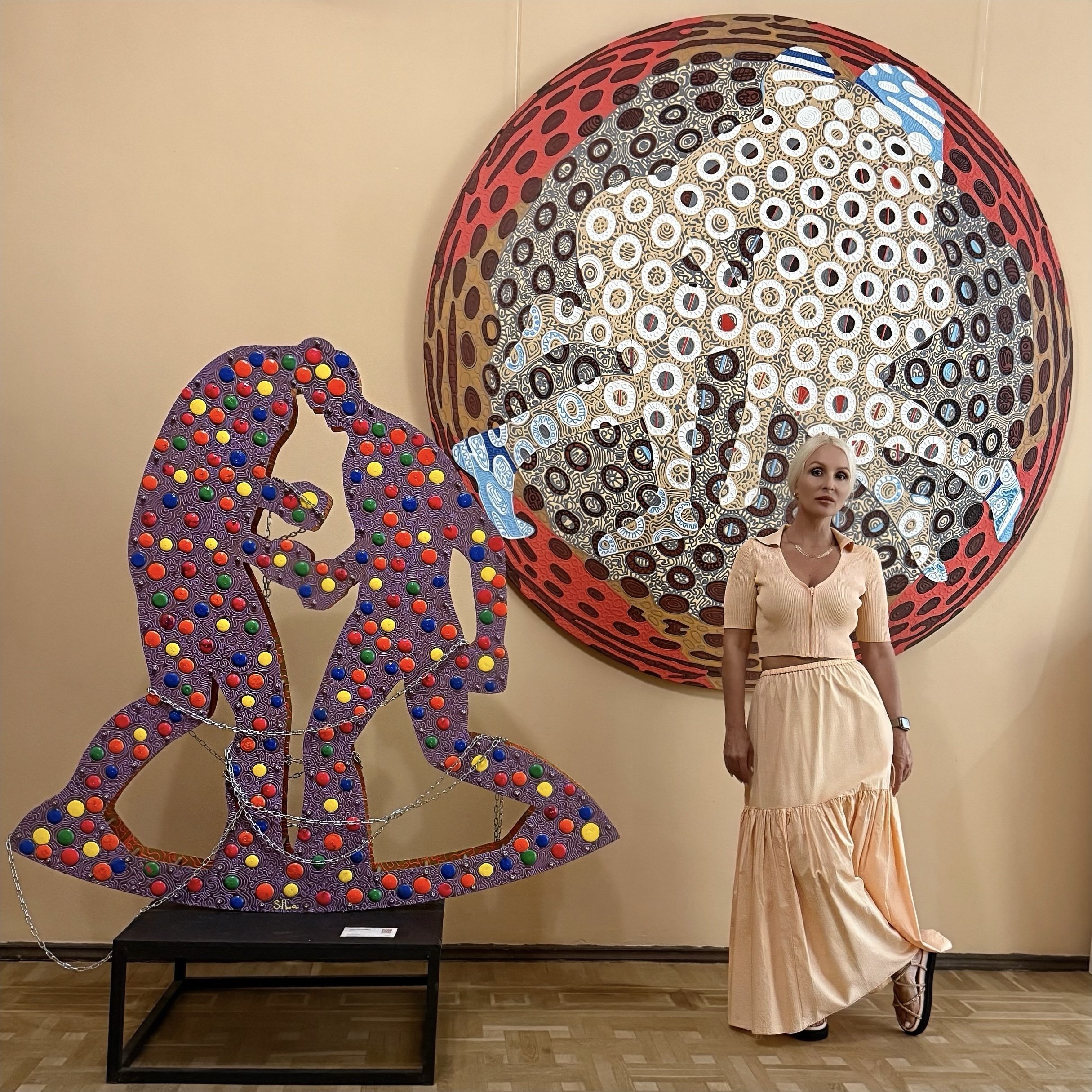 Contemporary artist Iryna Sushelnytska beside Moirai, a large circular painting, and You Are in the Game, a sculptural installation.