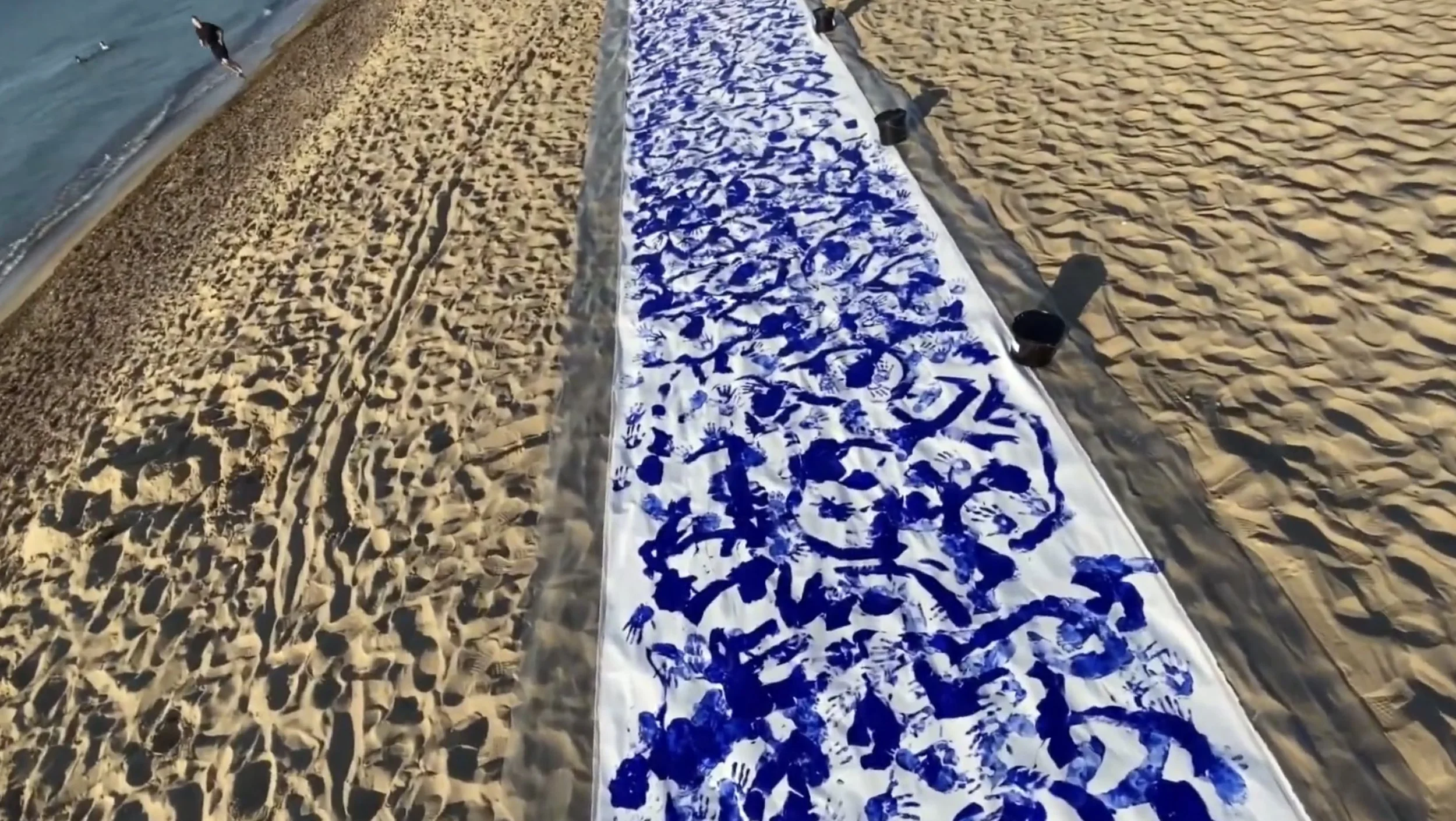 The continuous fifteen-metre canvas of Nine beside the sea, with blue bodily traces extending along its white surface.
