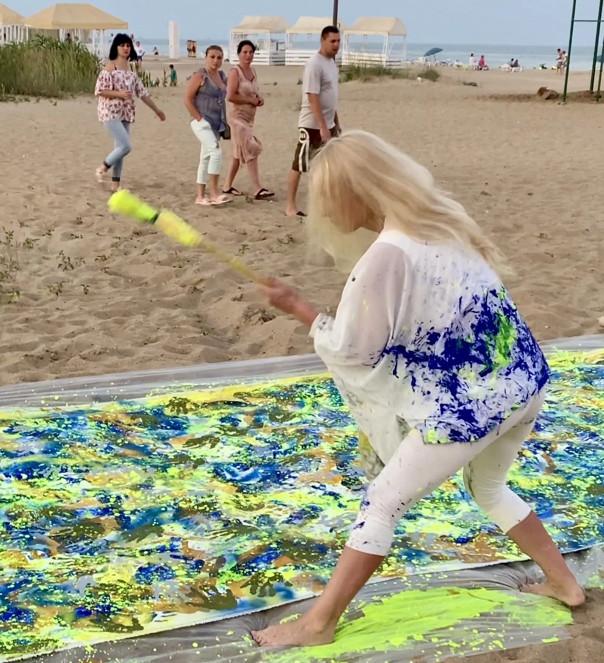 Iryna Sushelnytska applying fluorescent yellow paint to the canvas of Nine on the beach, with spectators watching behind her.
