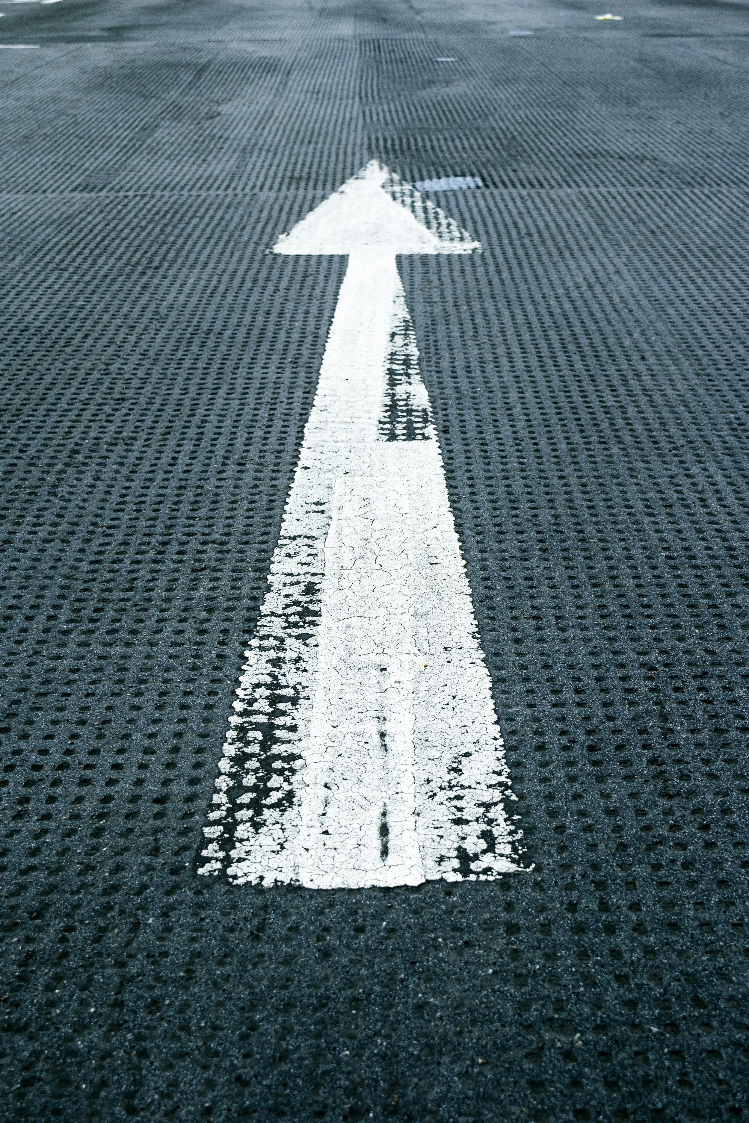 White arrow painted on a textured black asphalt road surface, pointing forward.