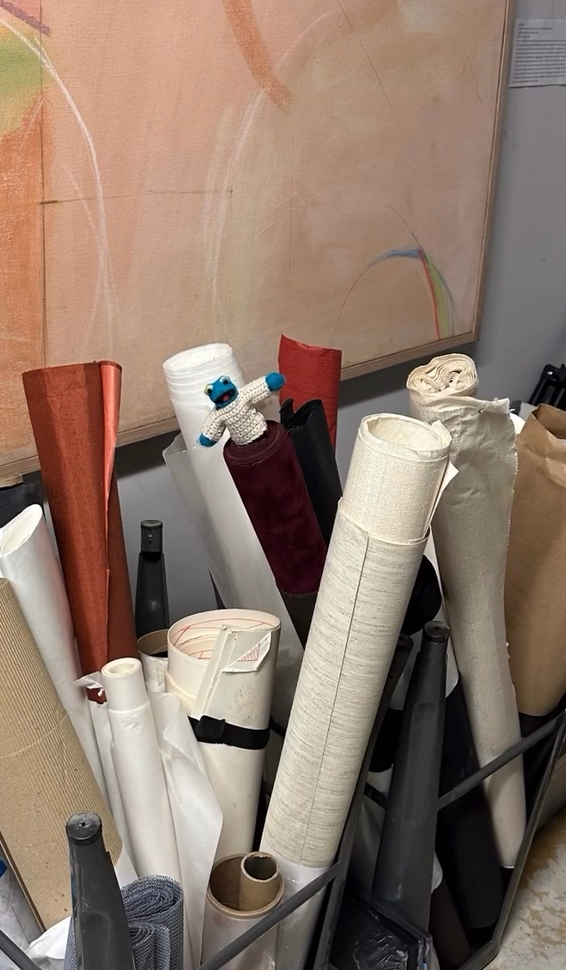 Collection of fabric rolls and cones in various colors and sizes, with a small plush toy on top of a white roll, in an indoor setting.