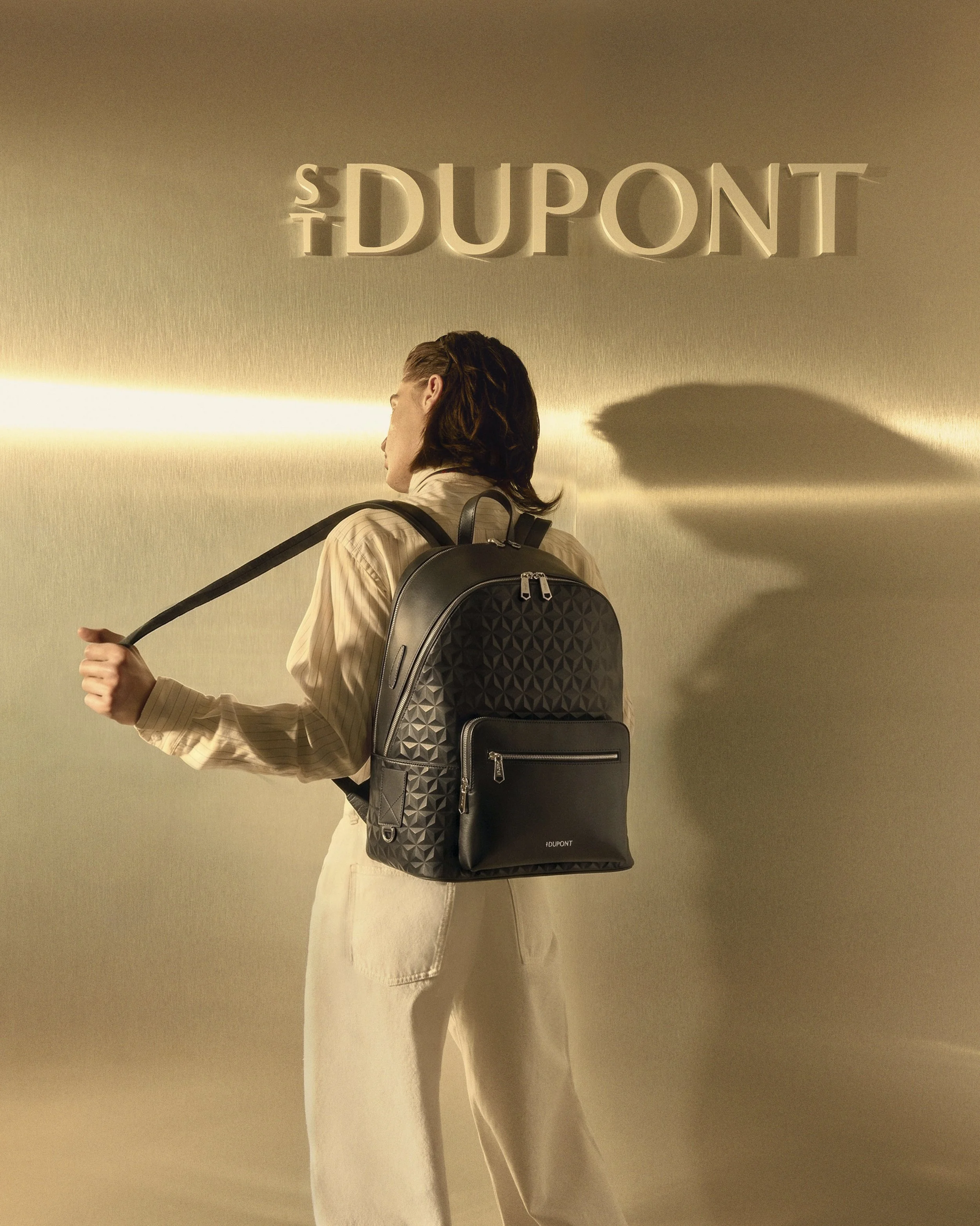 Pacôme Denim vu de dos porte un sac à dos APEX noir dans un décor architectural baigné de lumière.