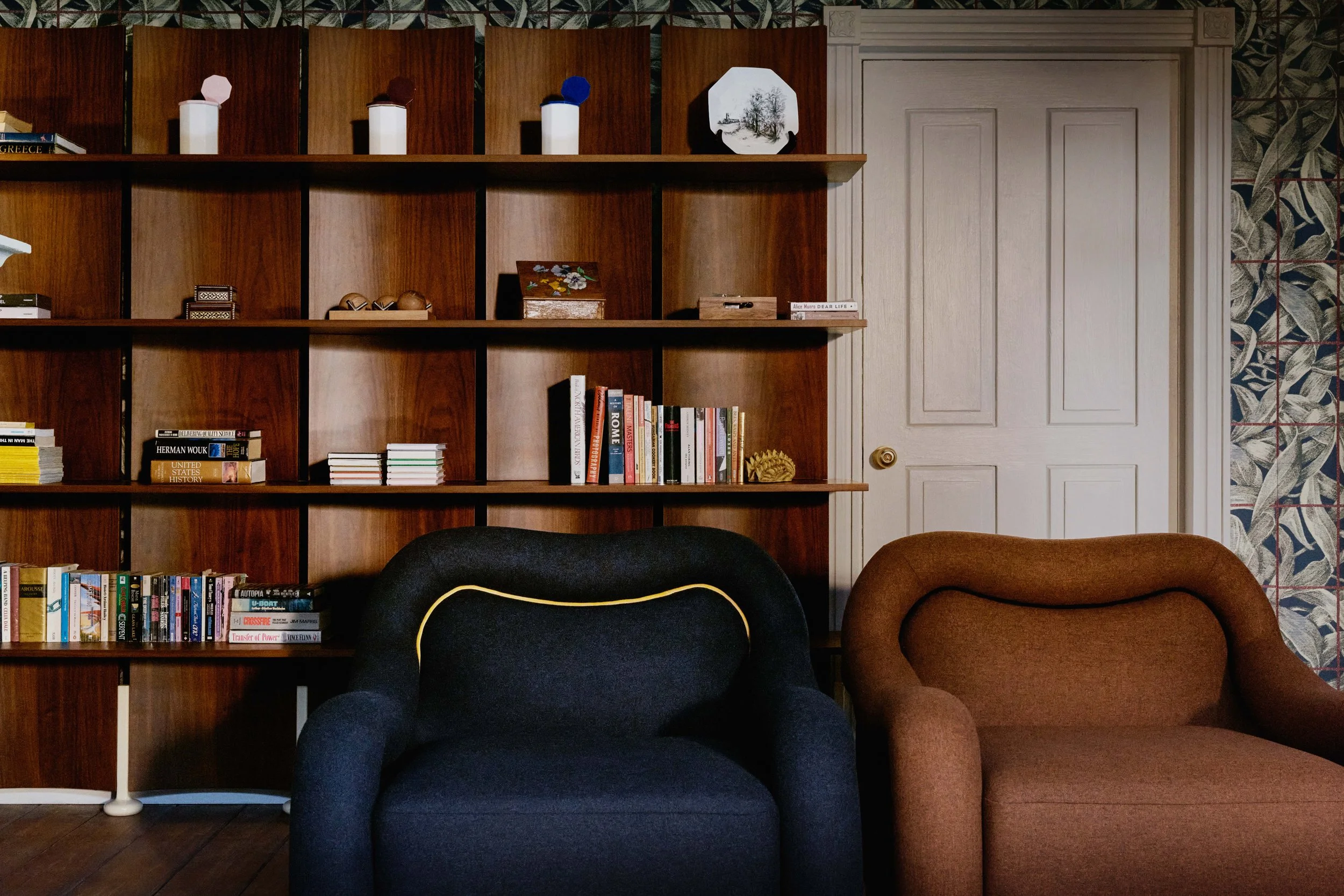 Fauteuils sombre et brun devant une bibliothèque en bois garnie de livres et d’objets, collection Atlas of Desire de Zara Home.