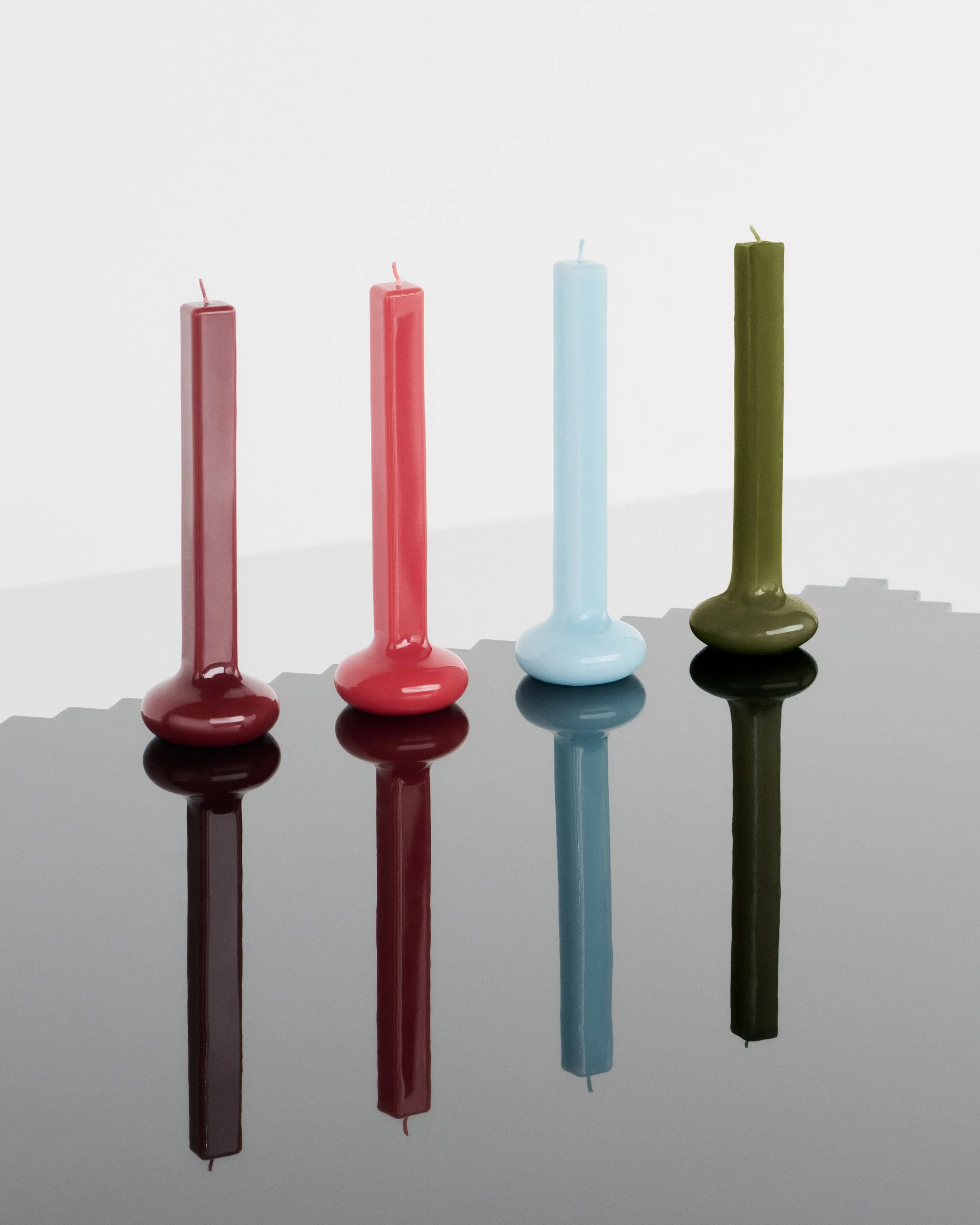 Quatre bougies élancées dans des supports assortis, aux teintes bordeaux, rouge, bleu clair et vert.