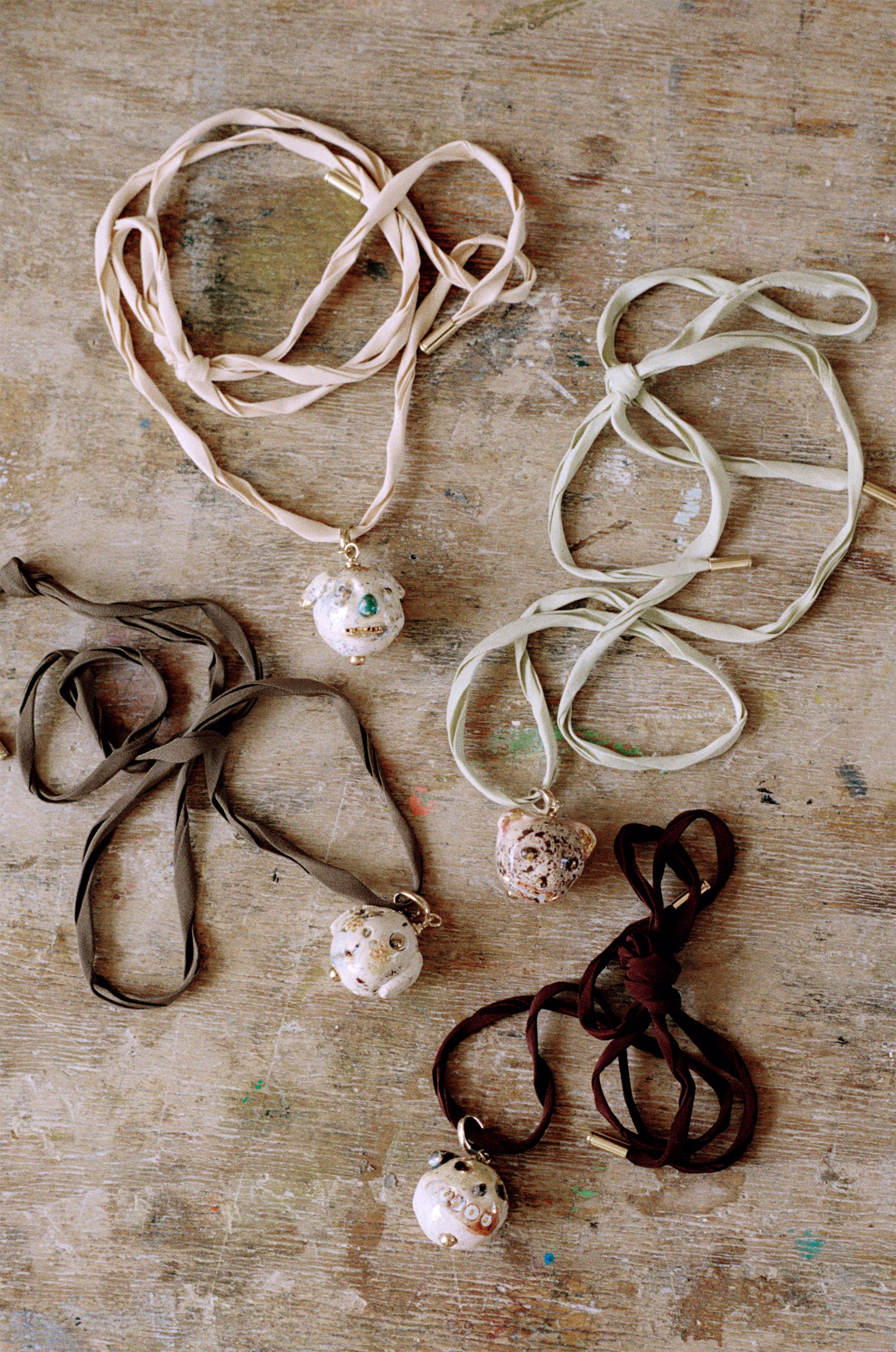 Quatre pendentifs Little Heads en céramique, suspendus à des liens textiles et disposés sur une table en bois.