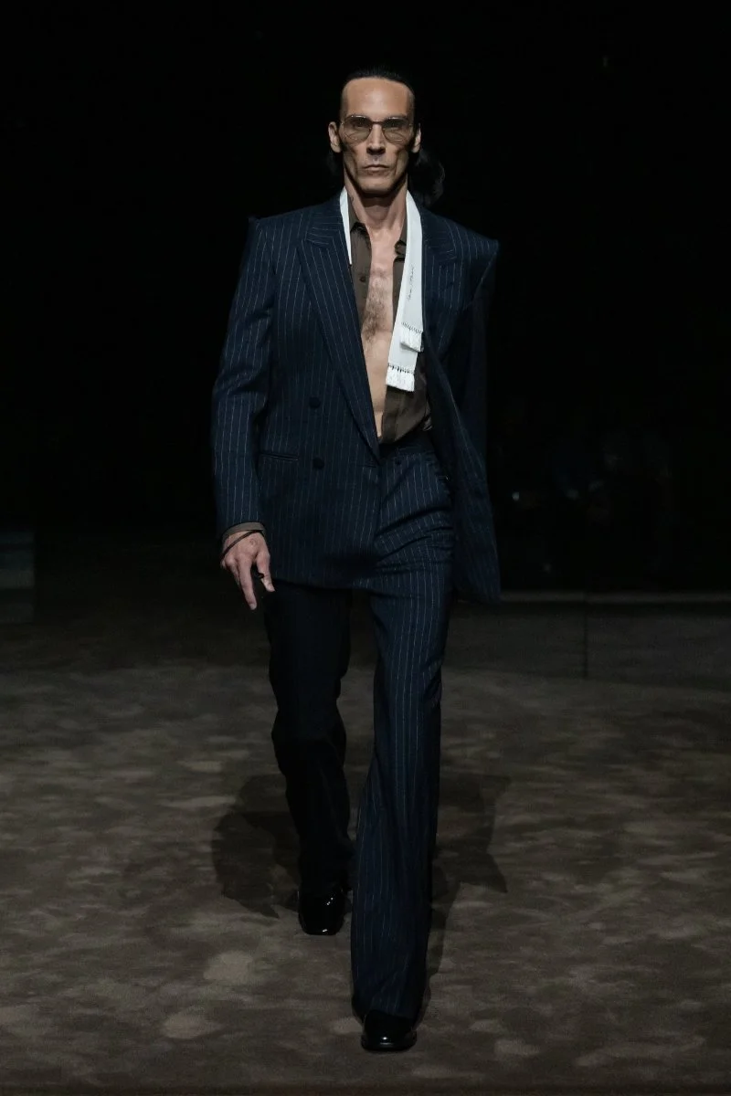 Mannequin en costume sombre et chemise blanche largement ouverte au défilé Tom Ford printemps-été 2027.