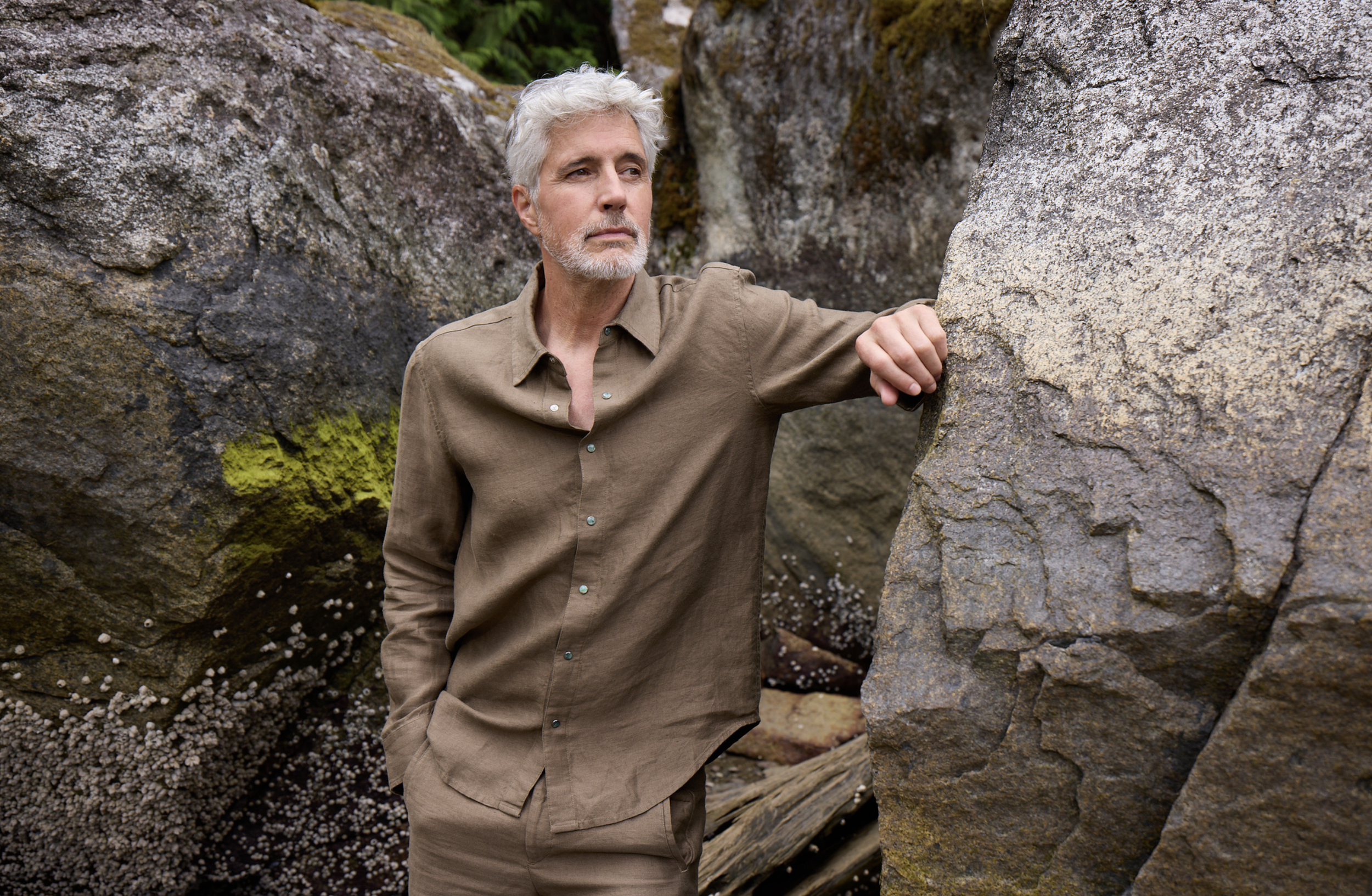 4. Homme en ensemble brun God’s True Cashmere photographié contre une paroi rocheuse.