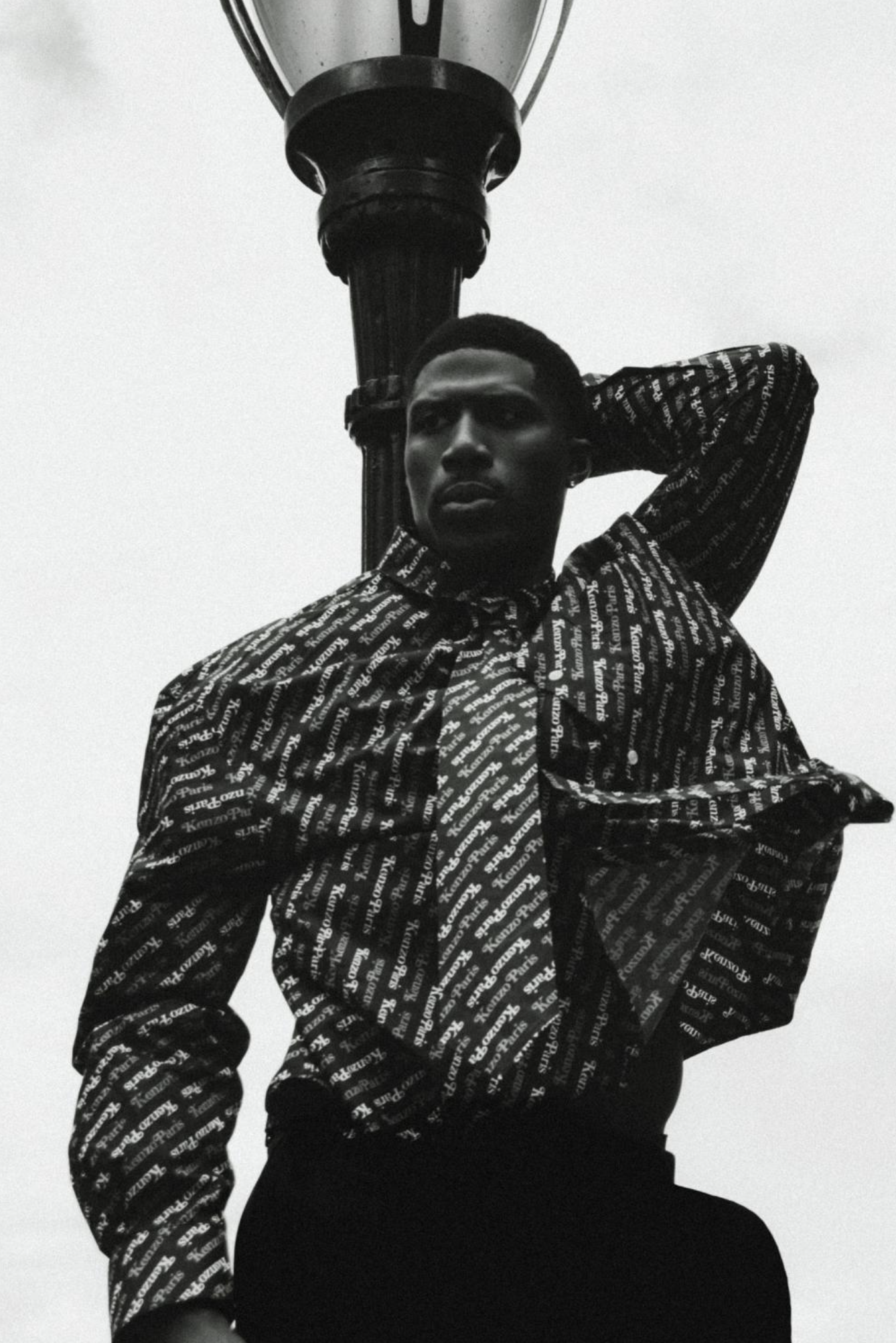 Akosa photographié en noir et blanc devant l’eau et la skyline new-yorkaise, vêtu d’un haut noir CELINE.