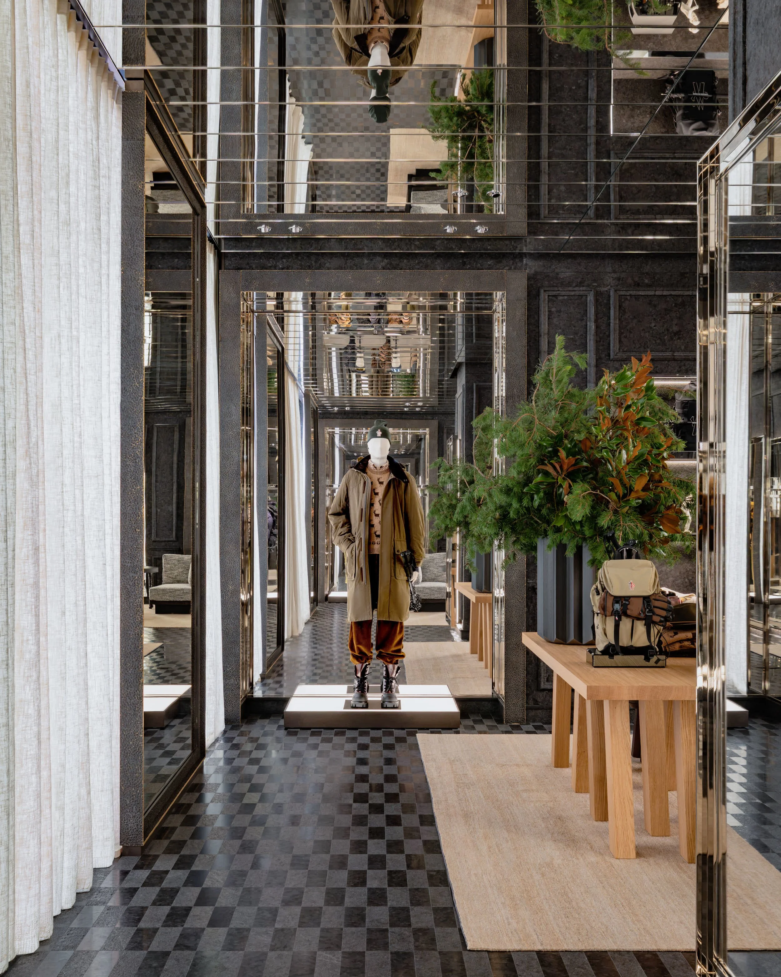 Perspective dans la boutique Moncler Fifth Avenue, entre de hautes baies vitrées, des présentoirs et des touches de végétation.