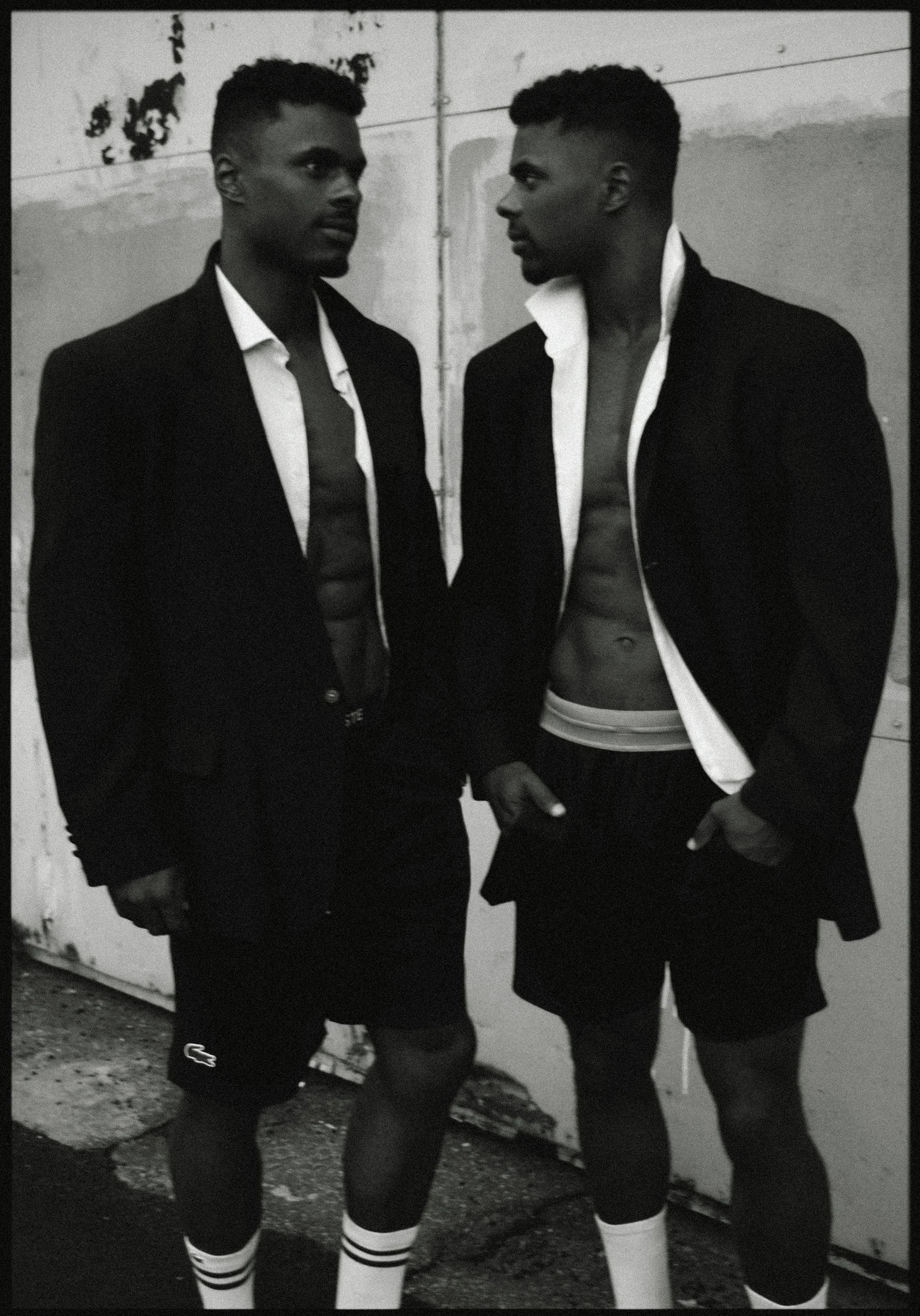 Charles et Maxence Bertimon en vestes sombres, chemises et shorts, photographiés debout l’un près de l’autre en noir et blanc.